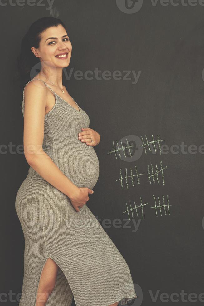 Portrait of pregnant woman in front of black chalkboard photo