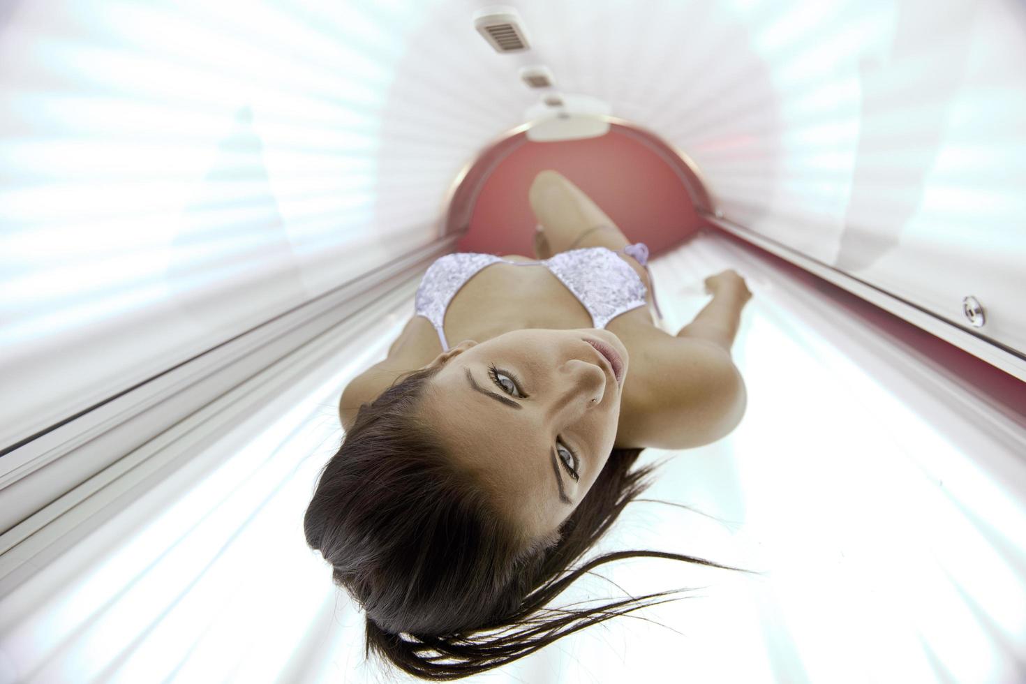 Beautiful young woman tanning in solarium photo