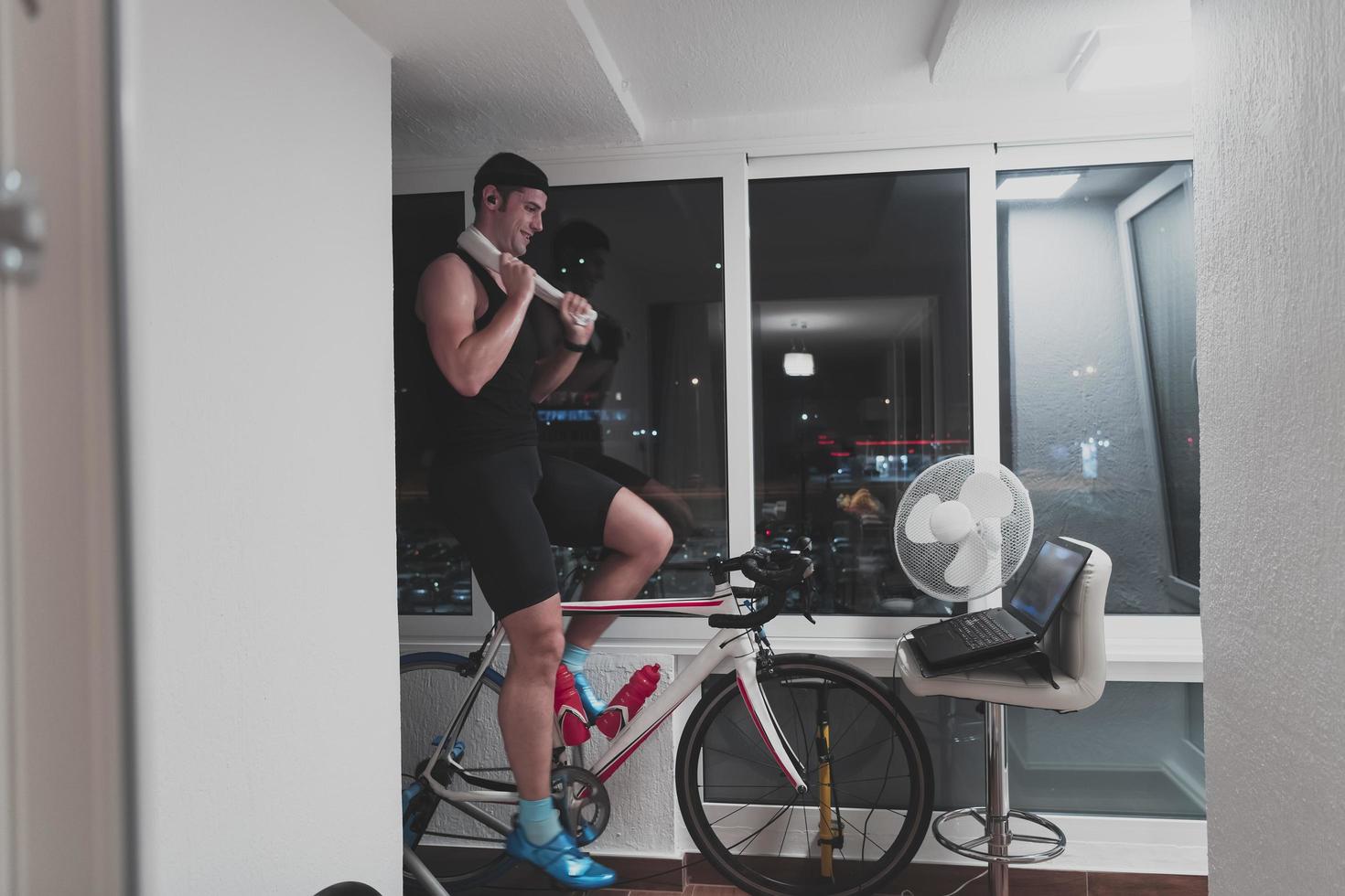 hombre en bicicleta en el entrenador de la máquina que está haciendo ejercicio en el hogar por la noche jugando al juego de carreras de bicicletas en línea foto