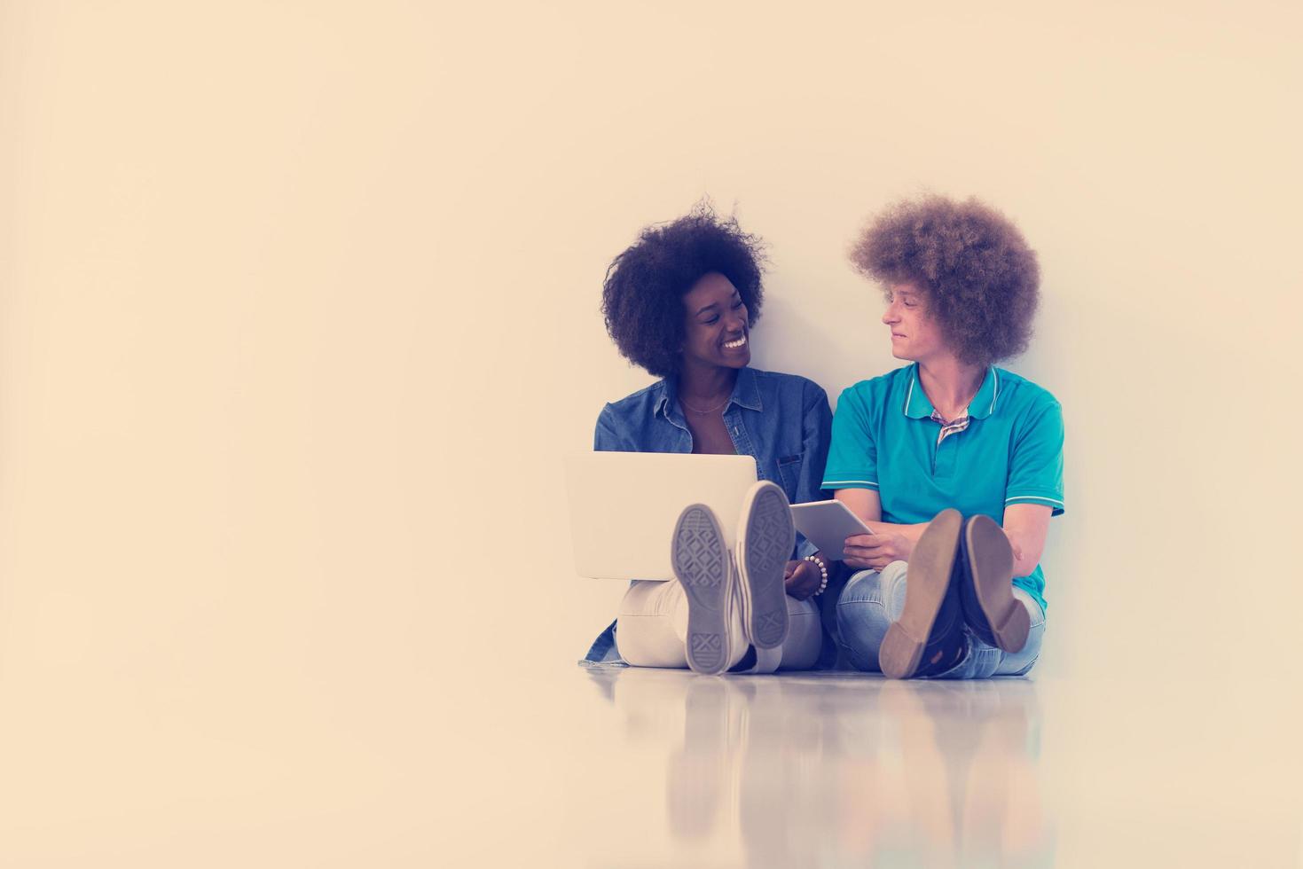 multiethnic couple sitting on the floor with a laptop and tablet photo