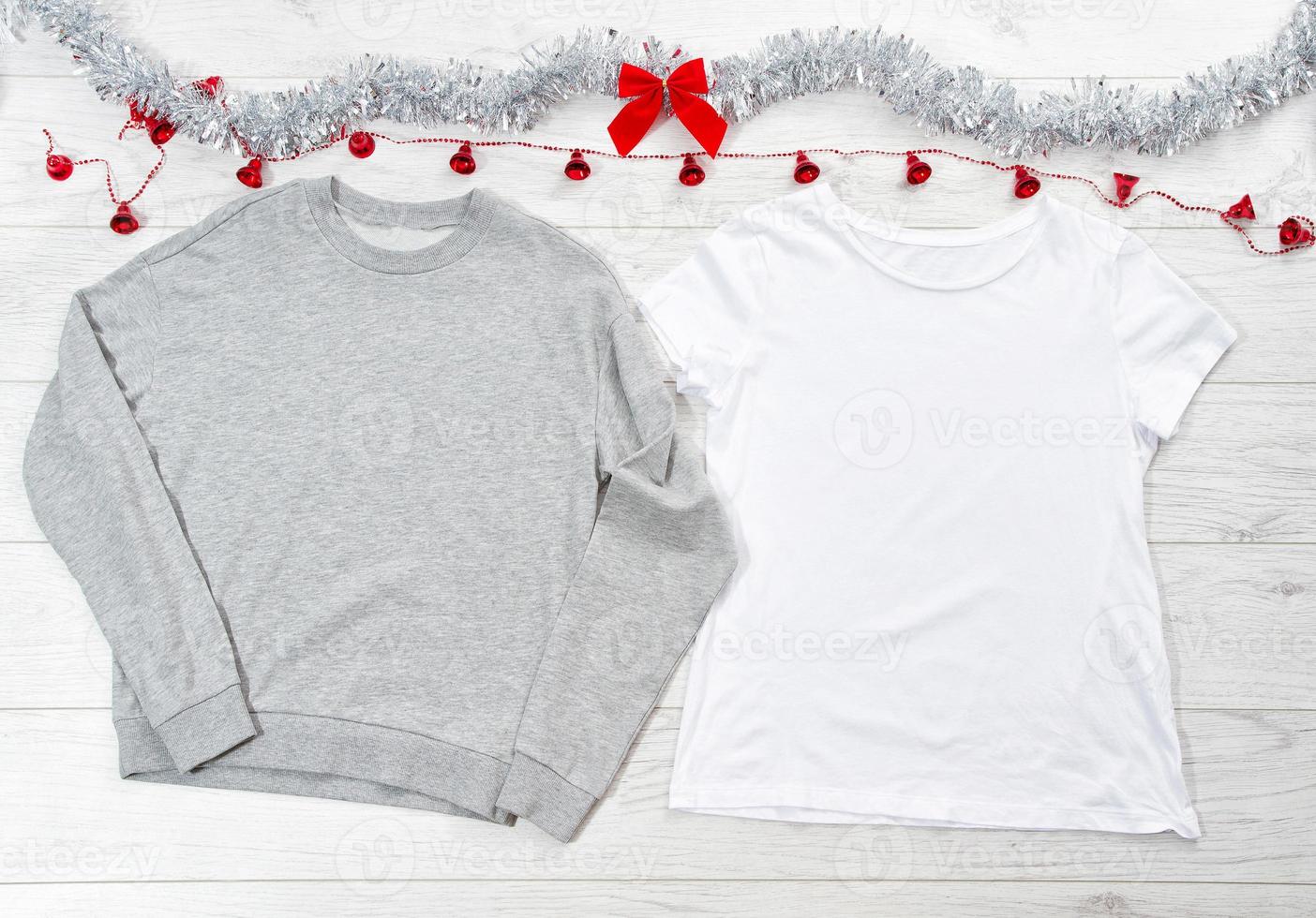 Close up white blank template t shirt, gray sweatshirt hoodie with copy space and Christmas Holiday concept. Top view mockup t-shirt, red bow on white wooden background. Happy New Year decorations photo