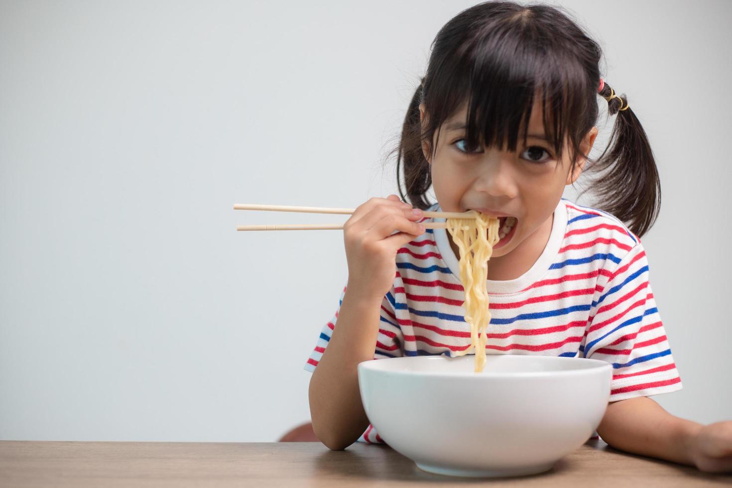 linda niña asiática comiendo deliciosos fideos instantáneos en casa. foto
