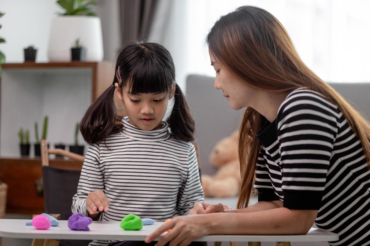 Asian mother and daughter play modeling clay together in kitchen with day light and they look happy. Concept of enjoy with family time photo