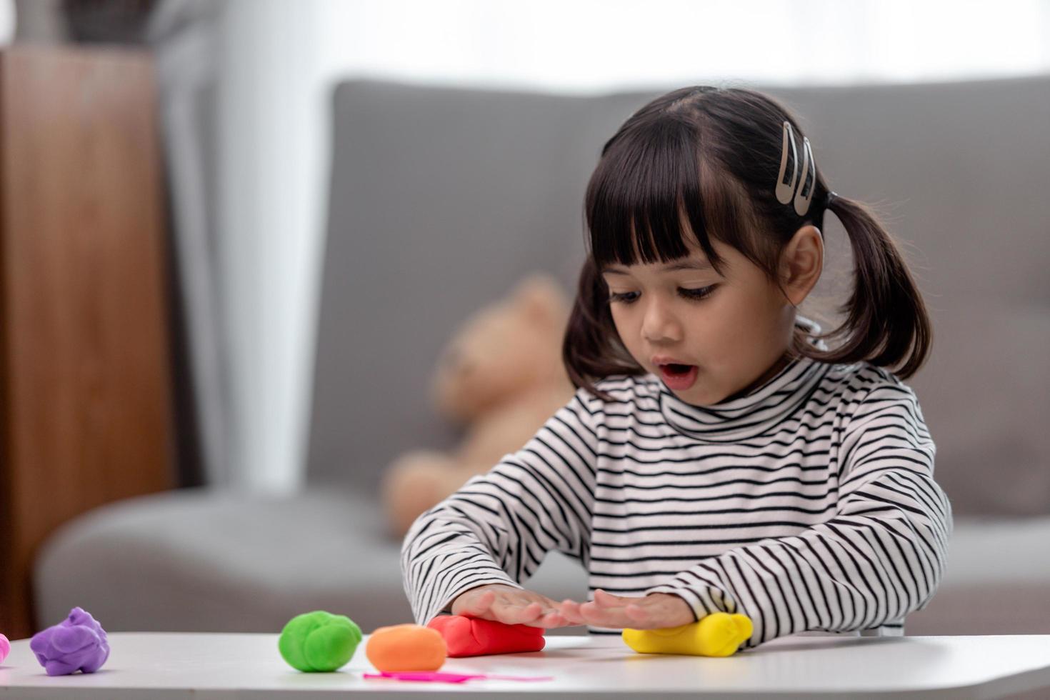 The little girl is learning to use colorful play dough in a well lit room photo