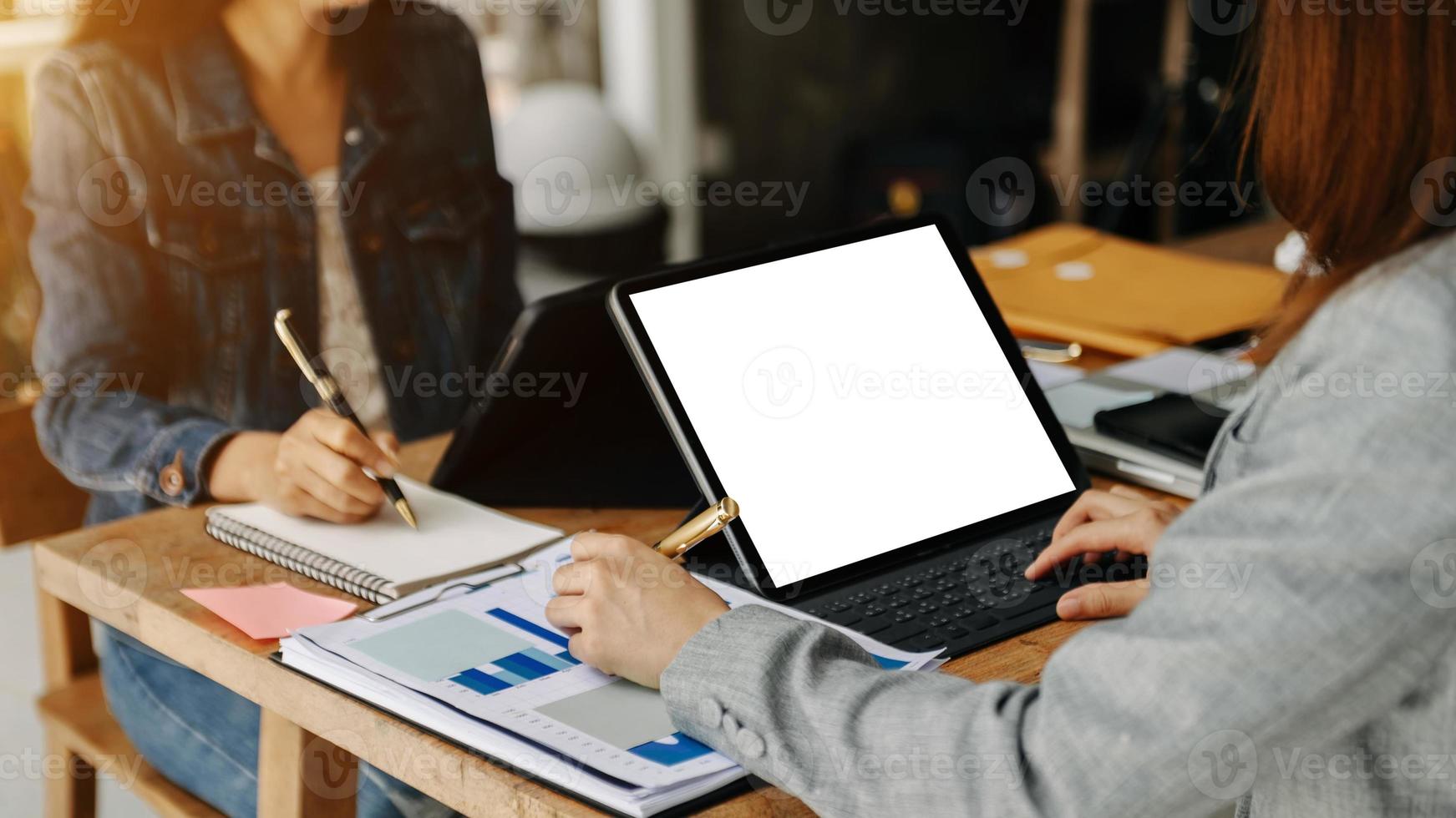 People using and looking at mockup laptop computer on wooden table together on office desk with clipping path tablet photo