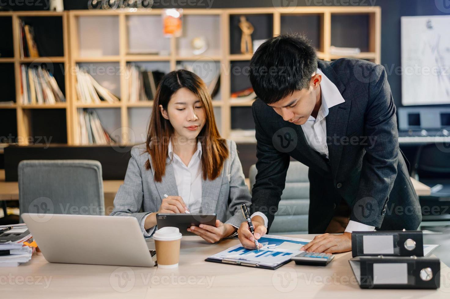 Asian business colleague business presents and explains and using laptop and tablet. Teamwork, financial marketing team,   while sitting in modern office room. photo