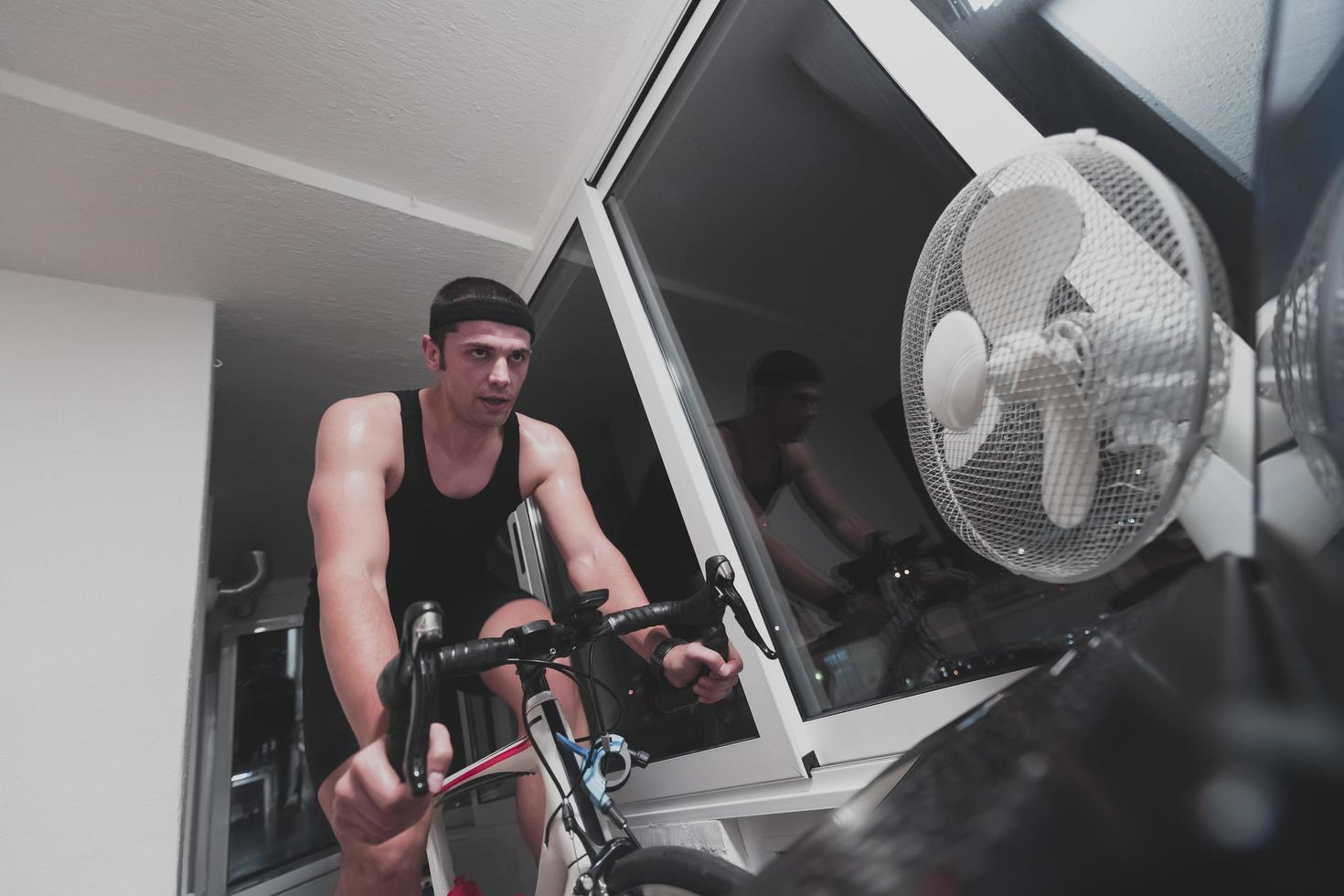 hombre en bicicleta en el entrenador de la máquina que está haciendo ejercicio en el hogar por la noche jugando al juego de carreras de bicicletas en línea foto