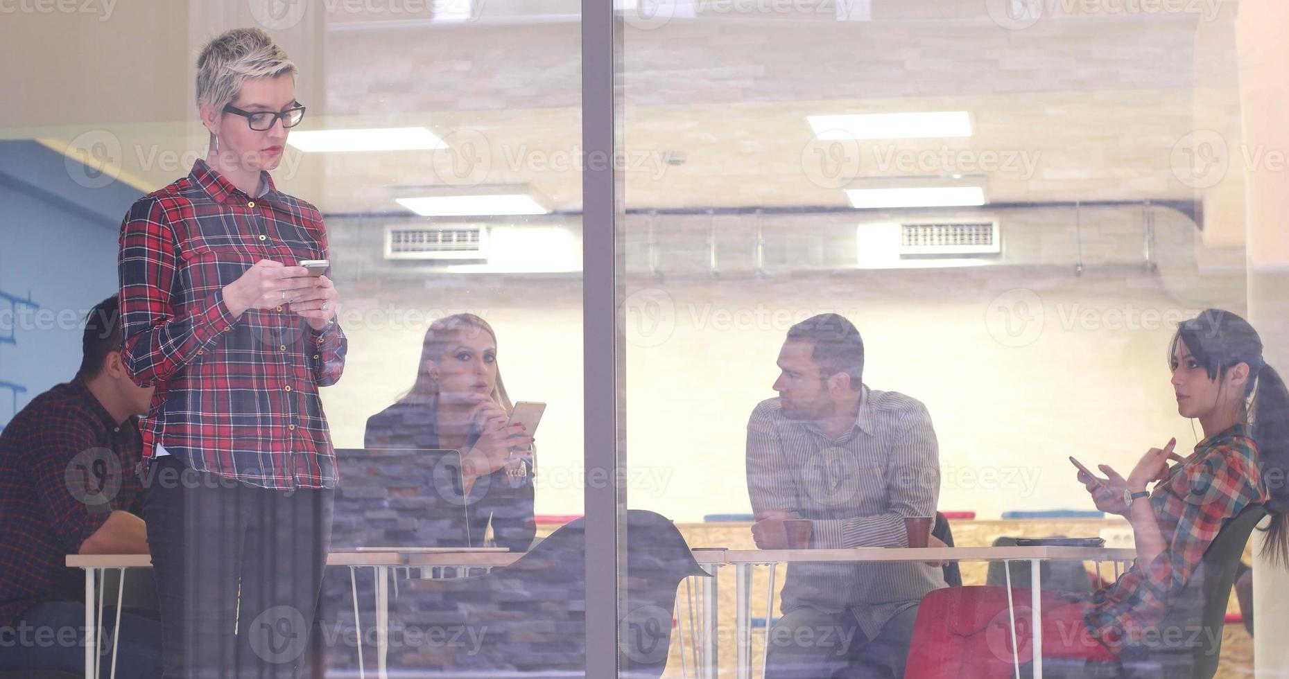 Business Woman Looking Through A Window And using On A Cell Phone during bussines meeting photo