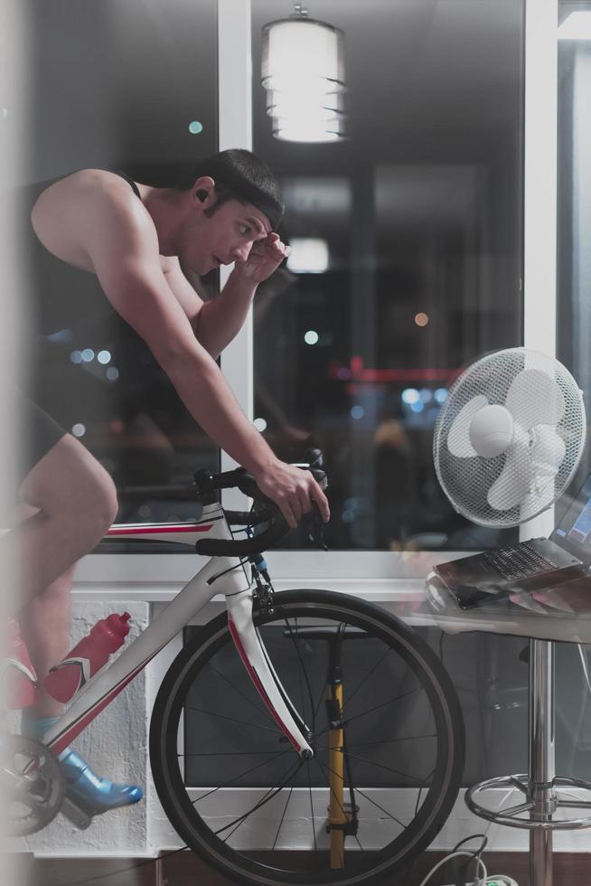 Man cycling on the machine trainer he is exercising in the home at night playing online bike racing game photo