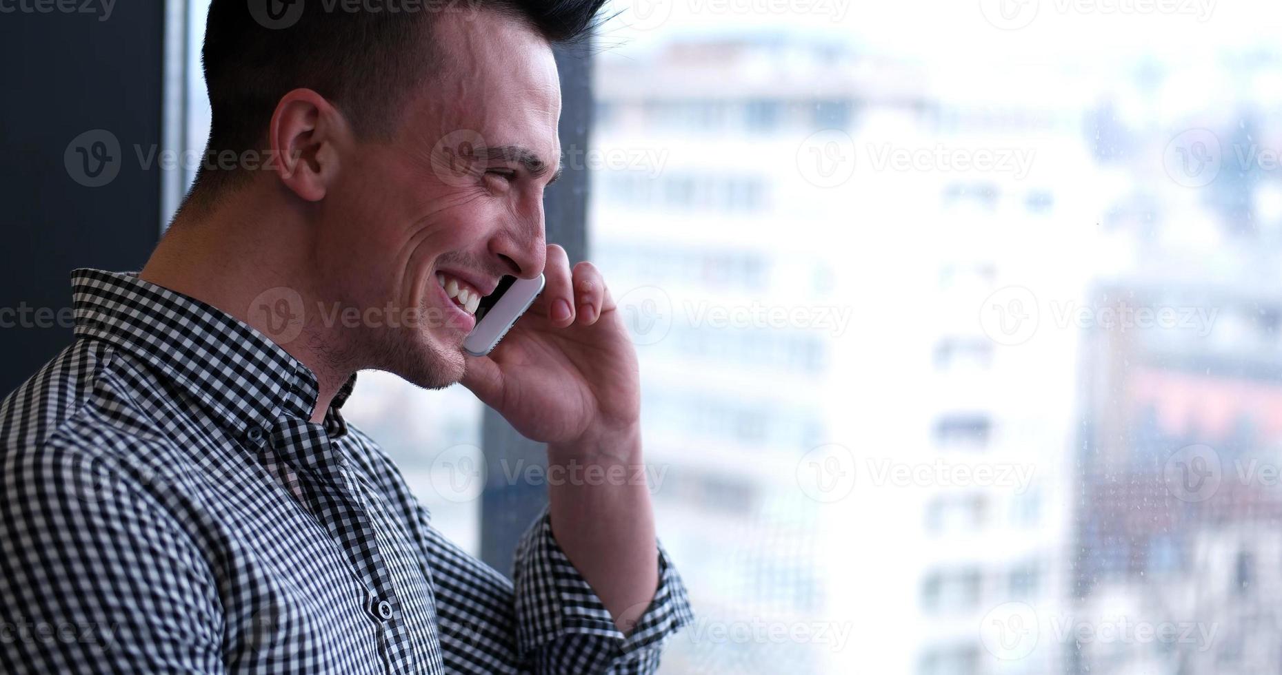 hombre de negocios hablando por teléfono celular, mirando por la ventana de la oficina foto