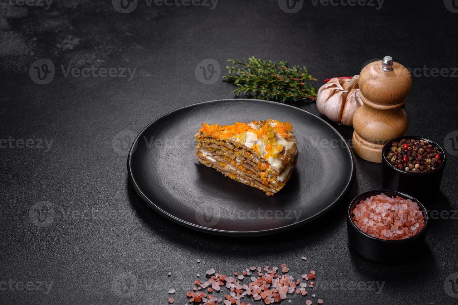 Delicious fresh liver cake with mayonnaise and carrots on a black plate against a dark concrete background photo