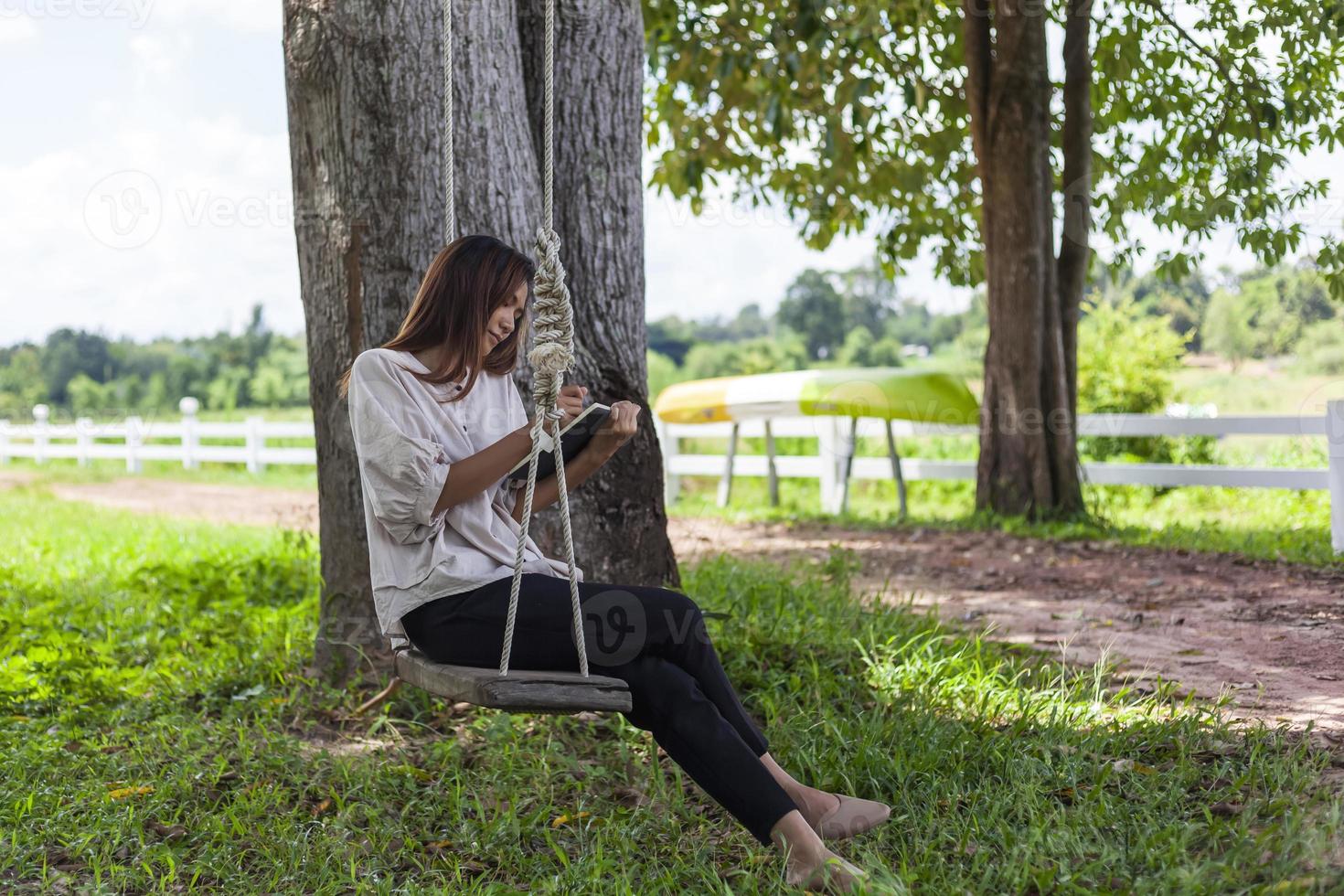Beautiful Asian woman sitting on a swing and writing something down in a notebook. photo