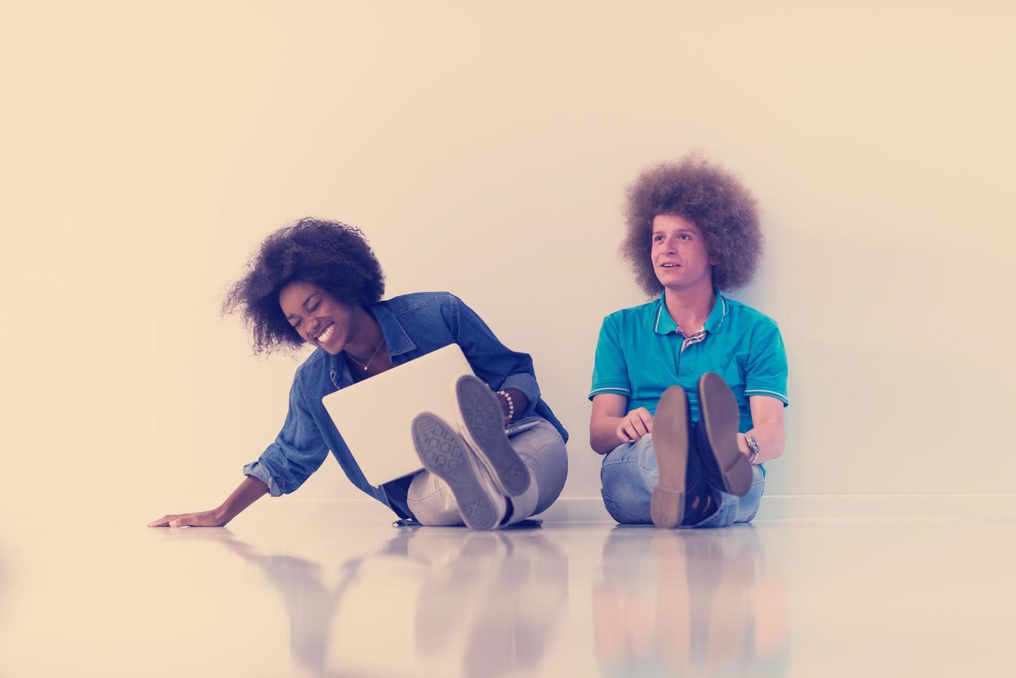 multiethnic couple sitting on the floor with a laptop and tablet photo