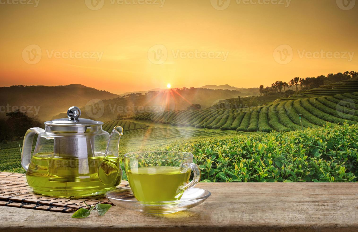taza de té verde caliente y jarras o frascos de vidrio y hojas de té reen sobre la mesa de madera y el fondo de las plantaciones de té foto