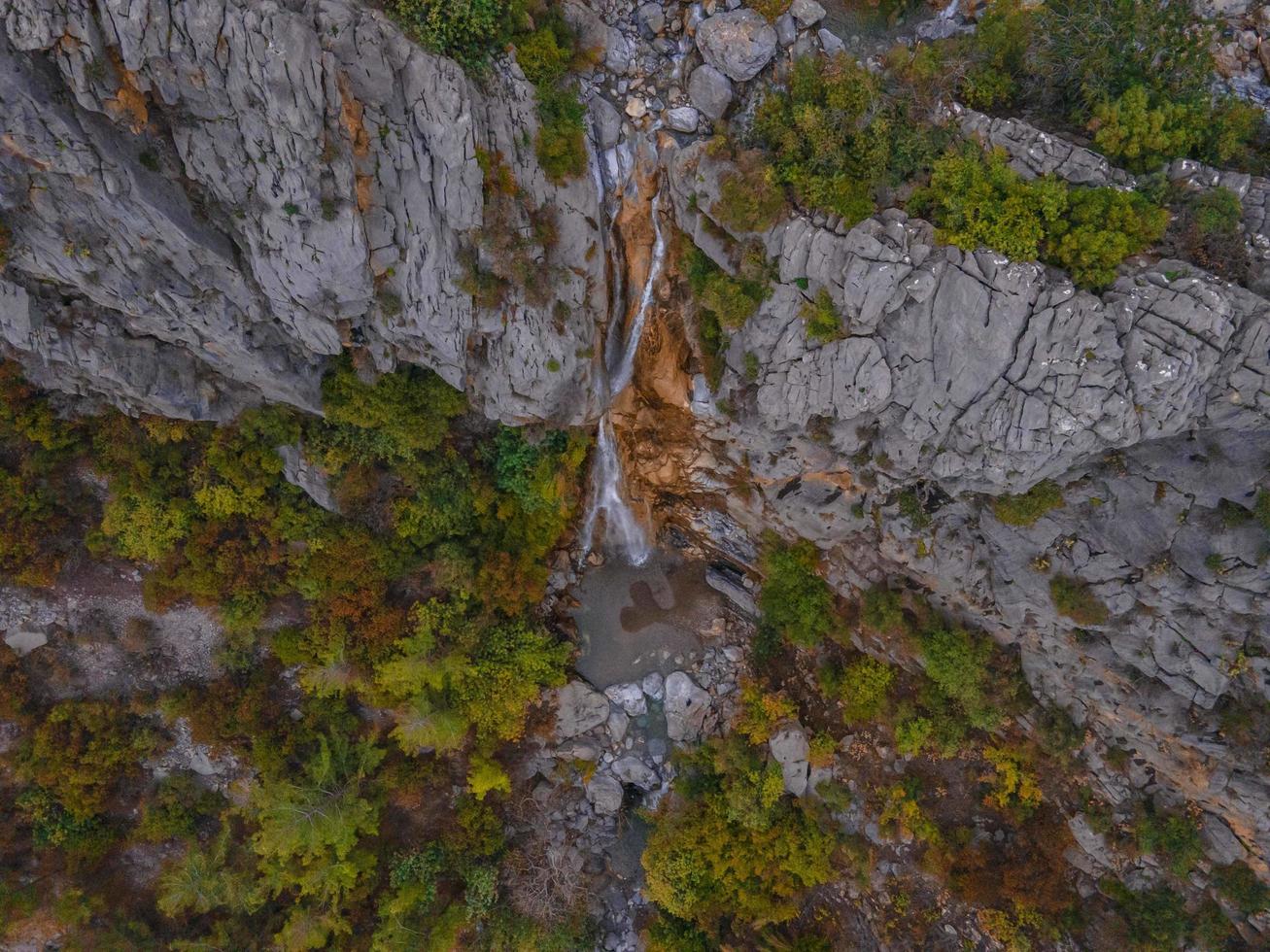 Mountain waterfall in a rocky gorge overgrown with green forest. Stream of icy water falls on mossy stones. photo