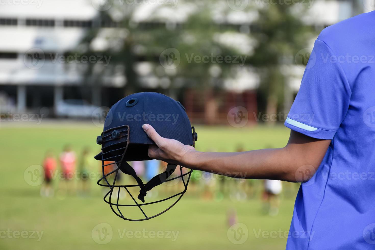 Cricket helmet holding in hand of cricketer, blurred green grass cricket field, concept for using cricket sport equipment in training. photo