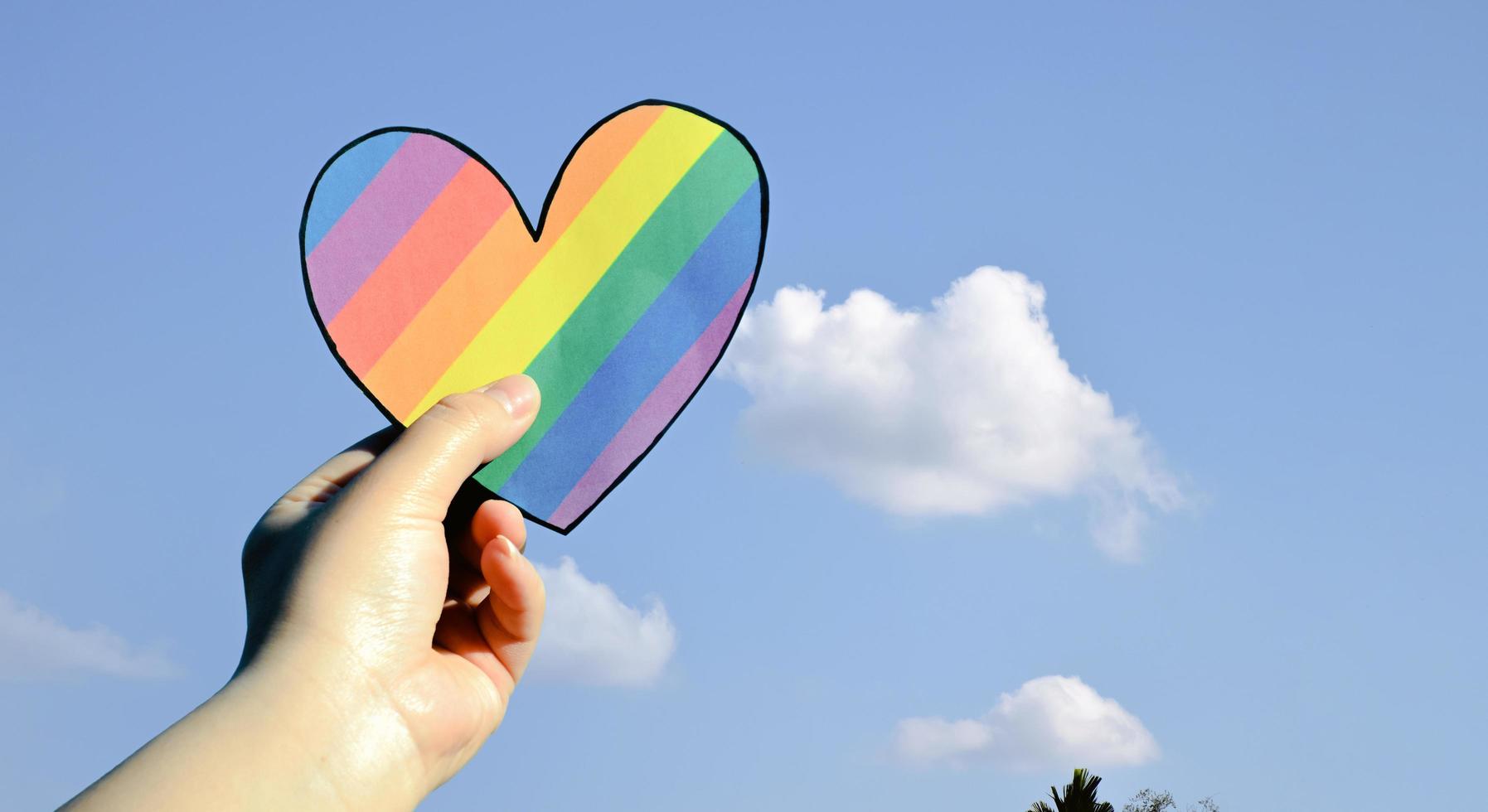 Two hearts made of rainbow colored paper are holding in hands of the LGBT person, concept for lgbtq communities celebrations in pride month around the world. photo