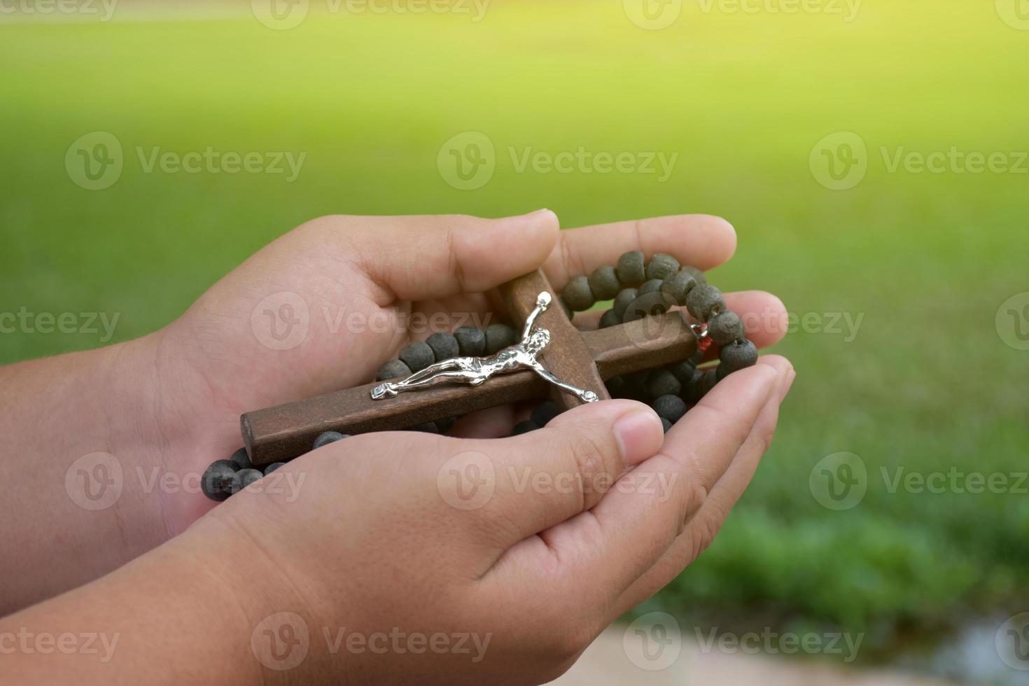 Wooden cross and wooden rosary are held in hands of young asian Catholic prayer while praying in the temple park area. photo