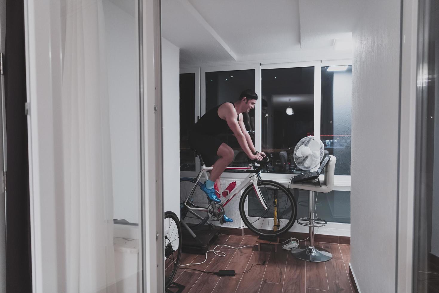 hombre en bicicleta en el entrenador de la máquina que está haciendo ejercicio en el hogar por la noche jugando al juego de carreras de bicicletas en línea foto