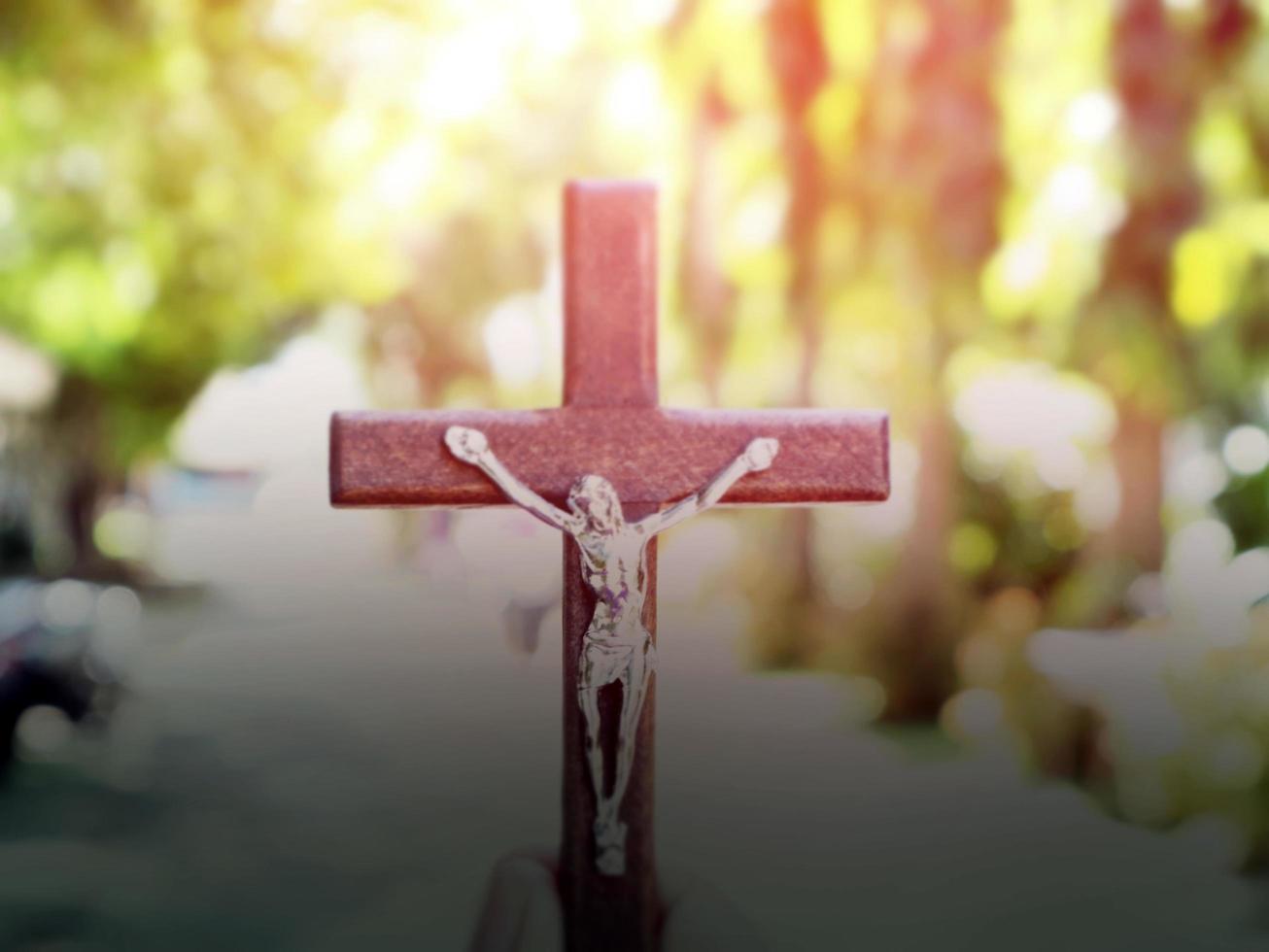 A black wooden cross with a statue of Jesus crucified by his arm. Behind it is the walk way of a school in an Asian country, soft and selective focus. photo