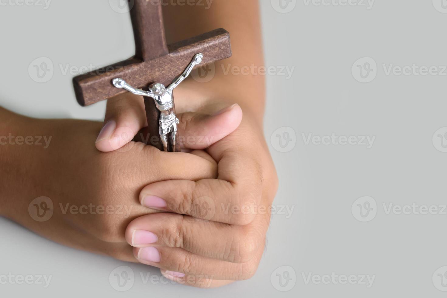 Wooden cross with a statue of Jesus crucified by his arm holding in hands of prayer on white table in the churce, soft and selective focus. photo