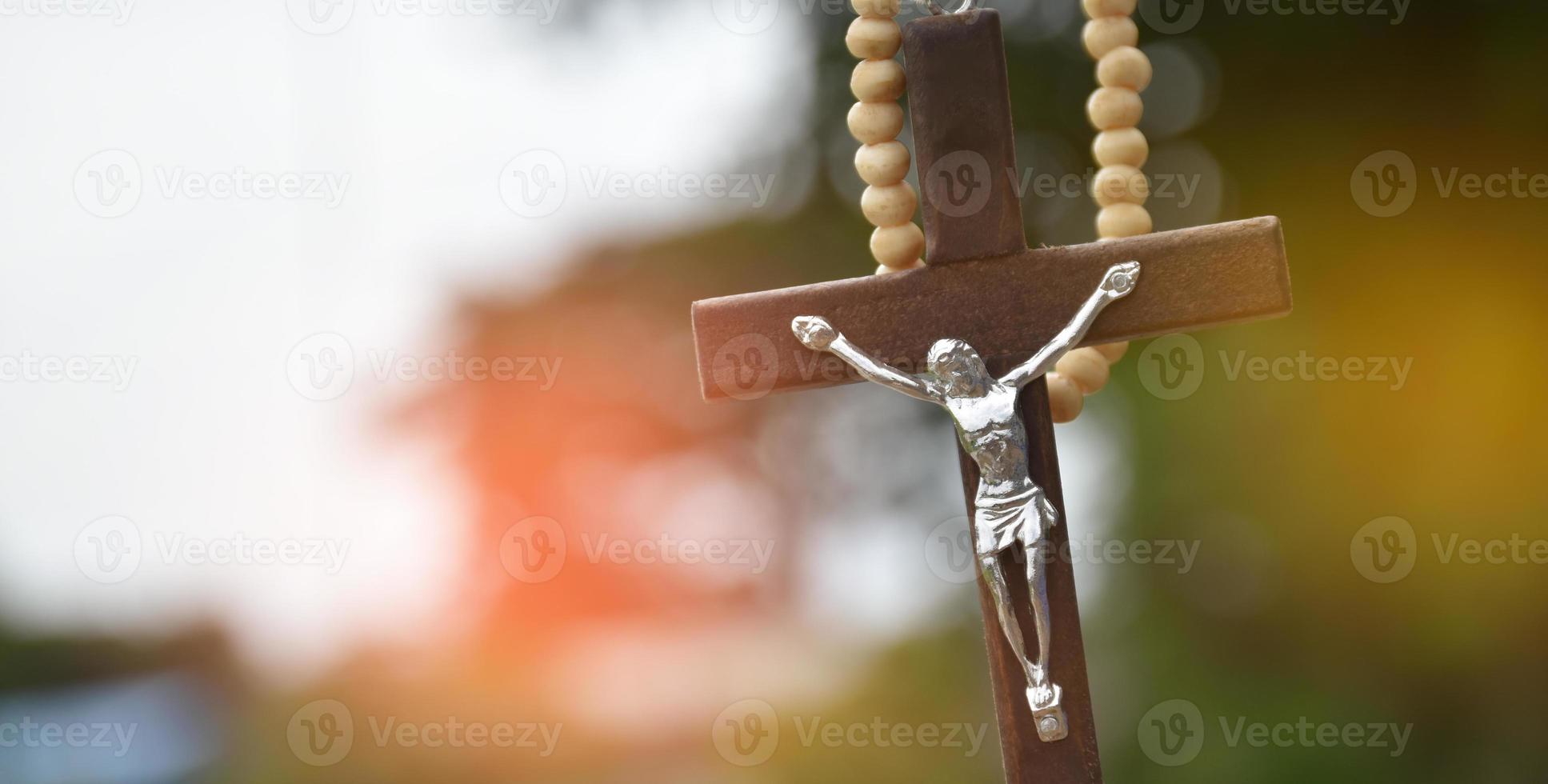 Wooden cross bead necklace hanging, natural blurr bokeh trees background, soft and selective focus. photo