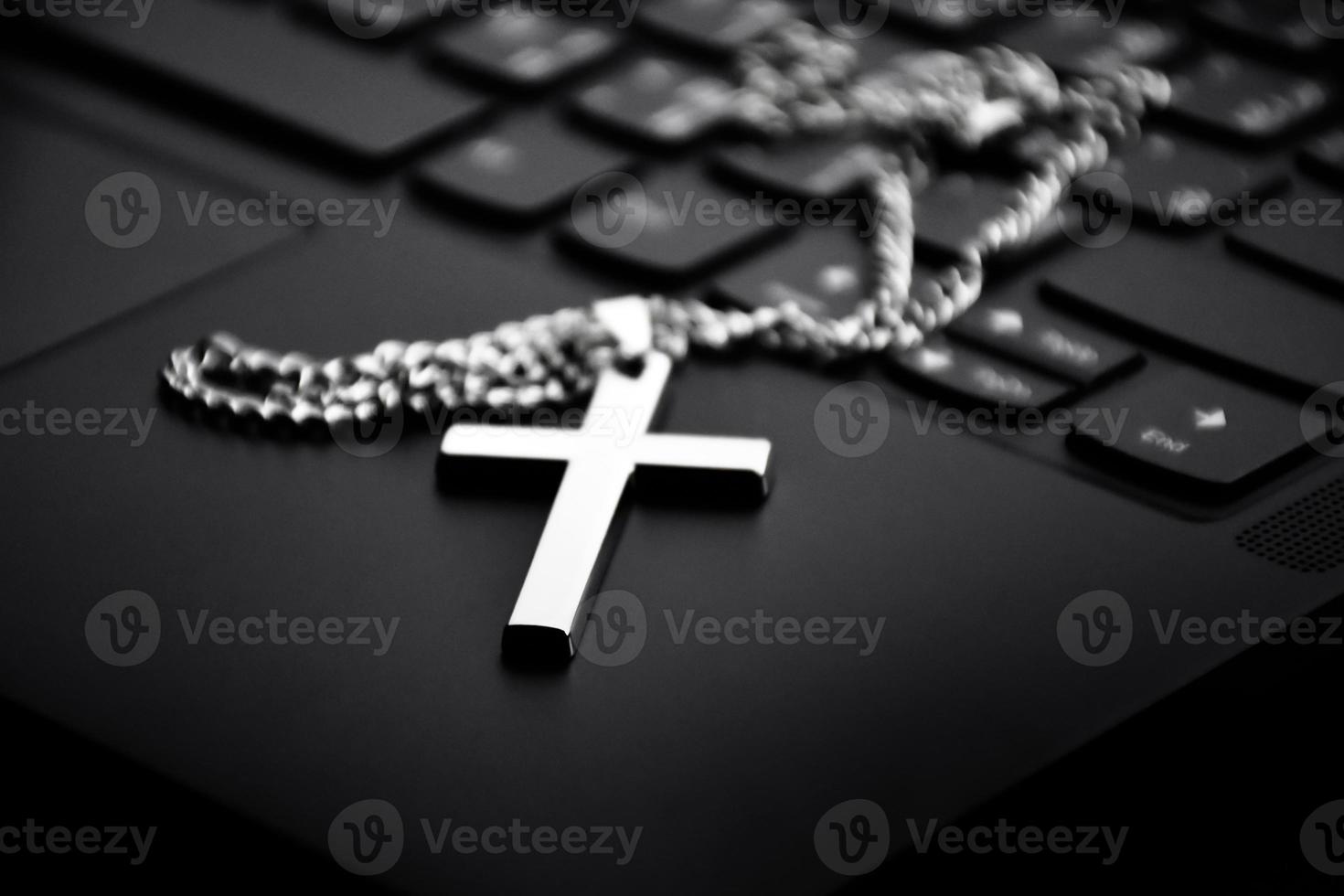 Metal cross necklace on notebook keyboard, soft and selective focus on cross necklace. photo