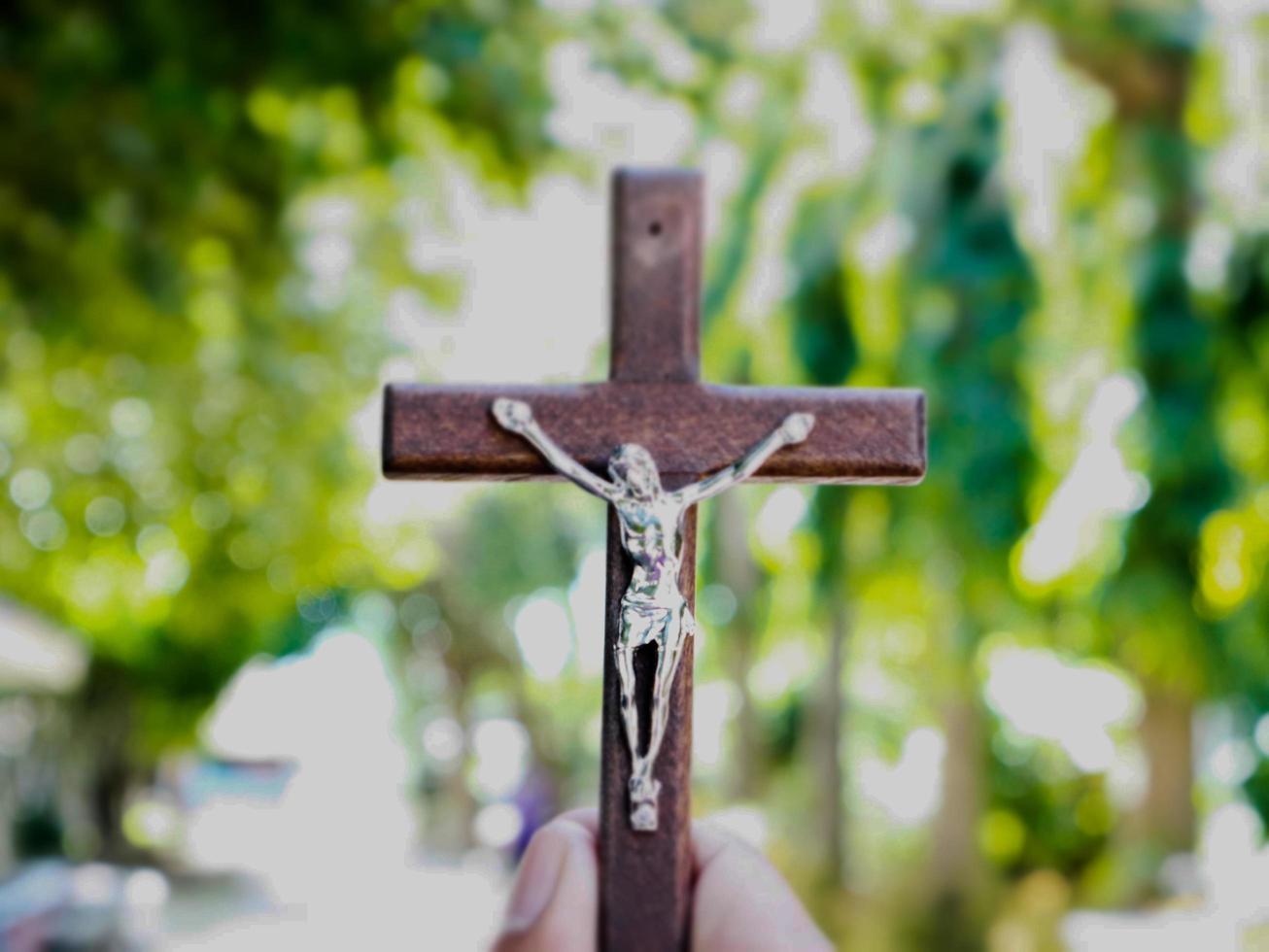 A black wooden cross with a statue of Jesus crucified by his arm. Behind it is the walk way of a school in an Asian country, soft and selective focus. photo