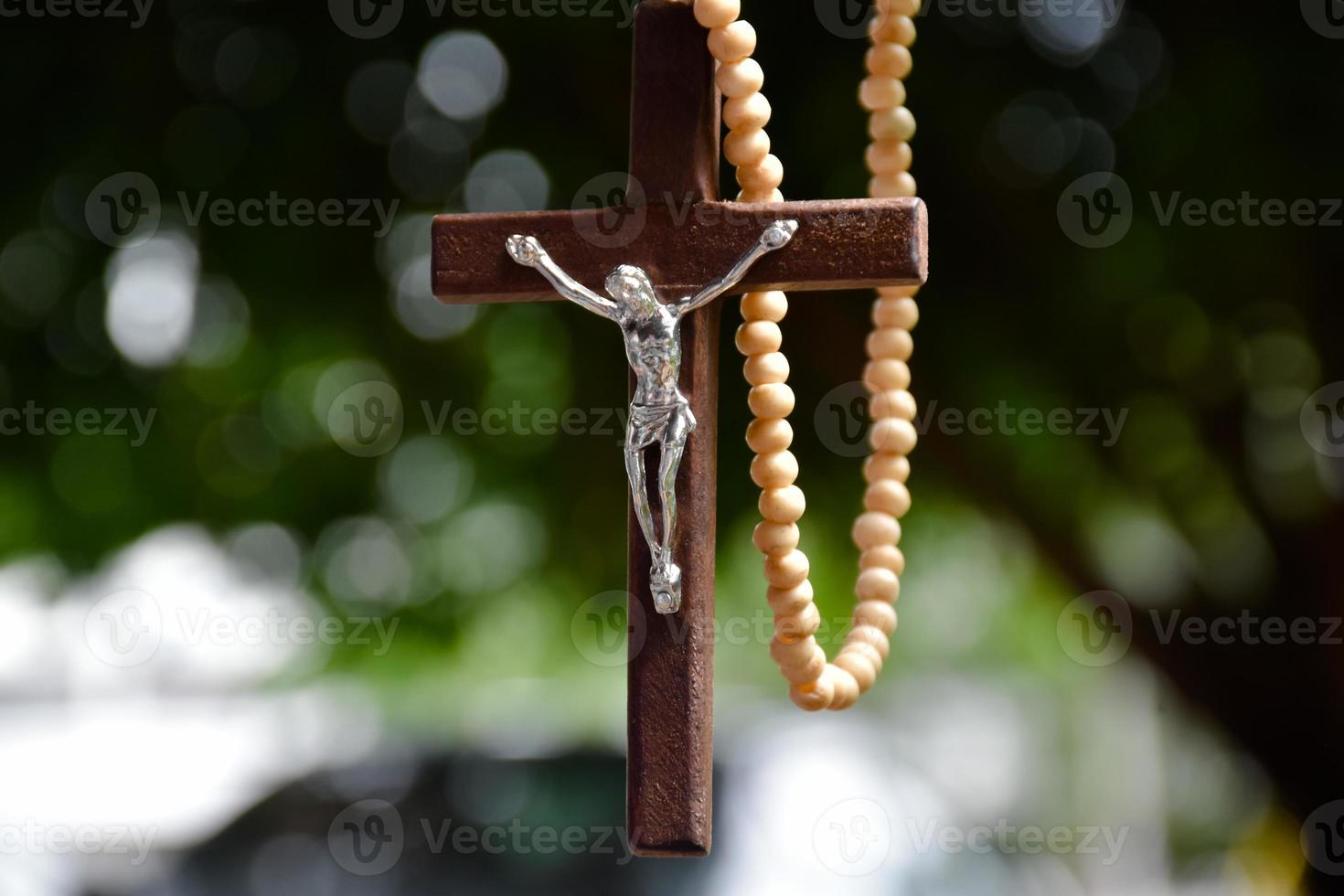 Wooden cross bead necklace hanging, natural blurr bokeh trees background, soft and selective focus. photo