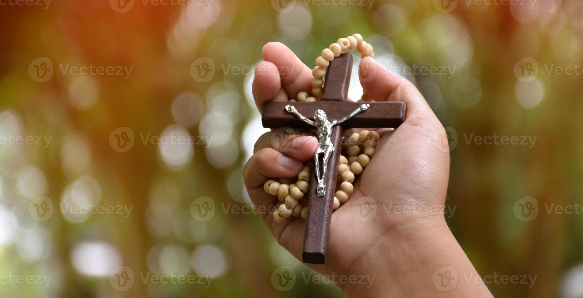 Wooden cross bead necklace holding in hands, natural blurr bokeh background, soft and selective focus. photo