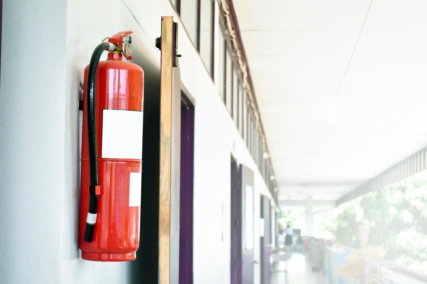 A red fire extinguisher is installed on a white cement wall in the front porch of the building to be used to extinguish a fire in the event of a building fire. photo