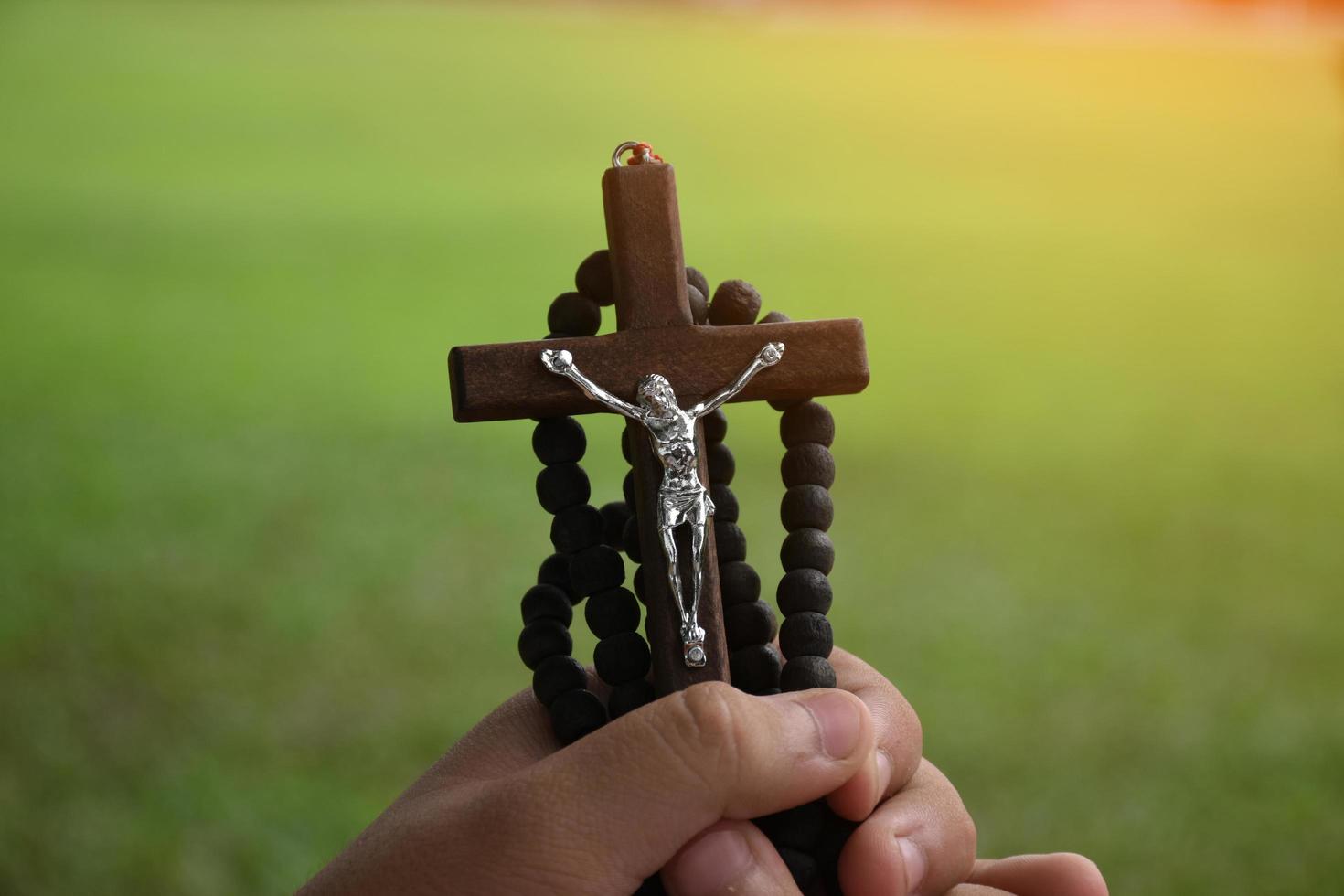 Wooden cross and wooden rosary are held in hands of young asian Catholic prayer while praying in the temple park area. photo