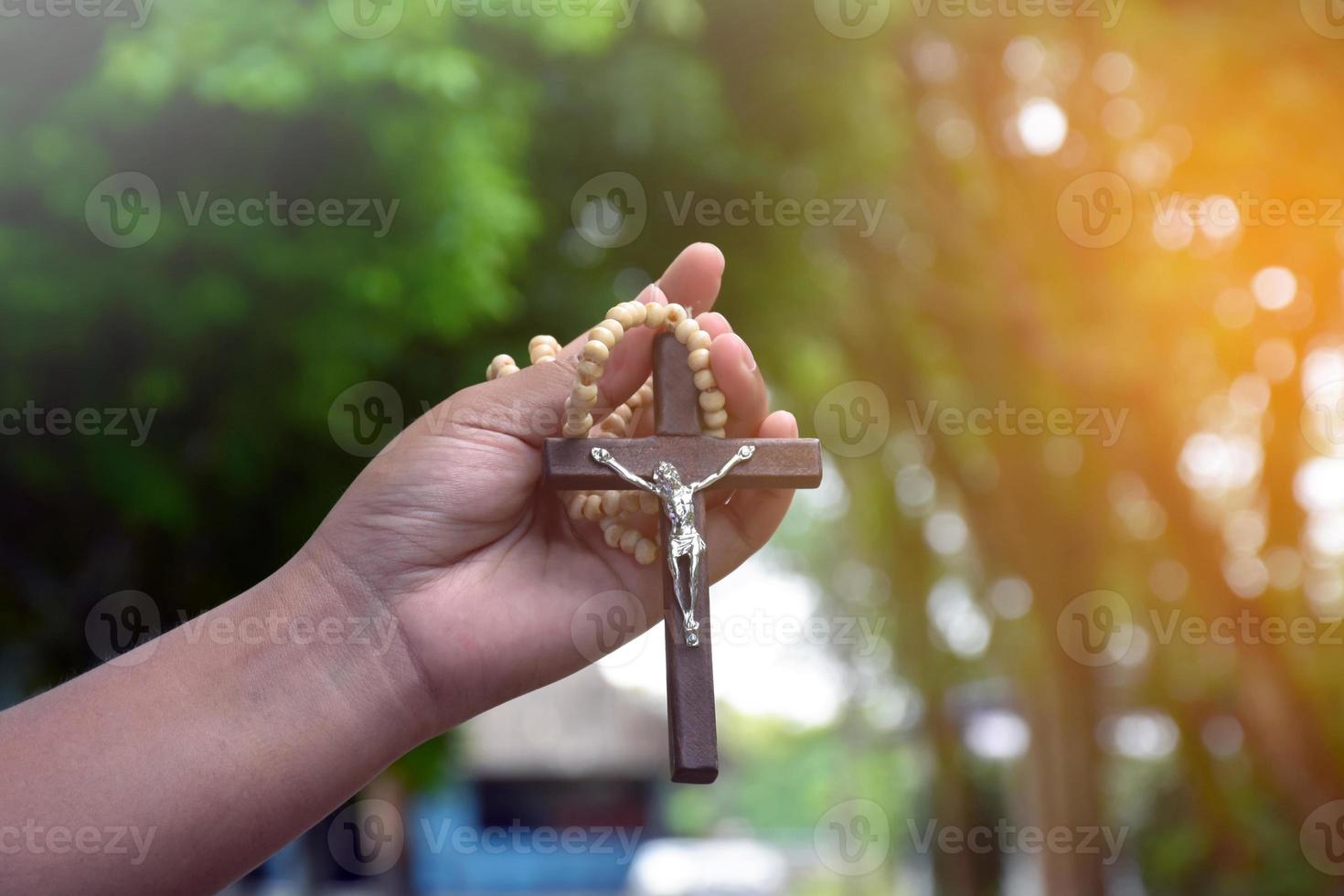 Wooden cross bead necklace holding in hands, natural blurr bokeh background, soft and selective focus. photo