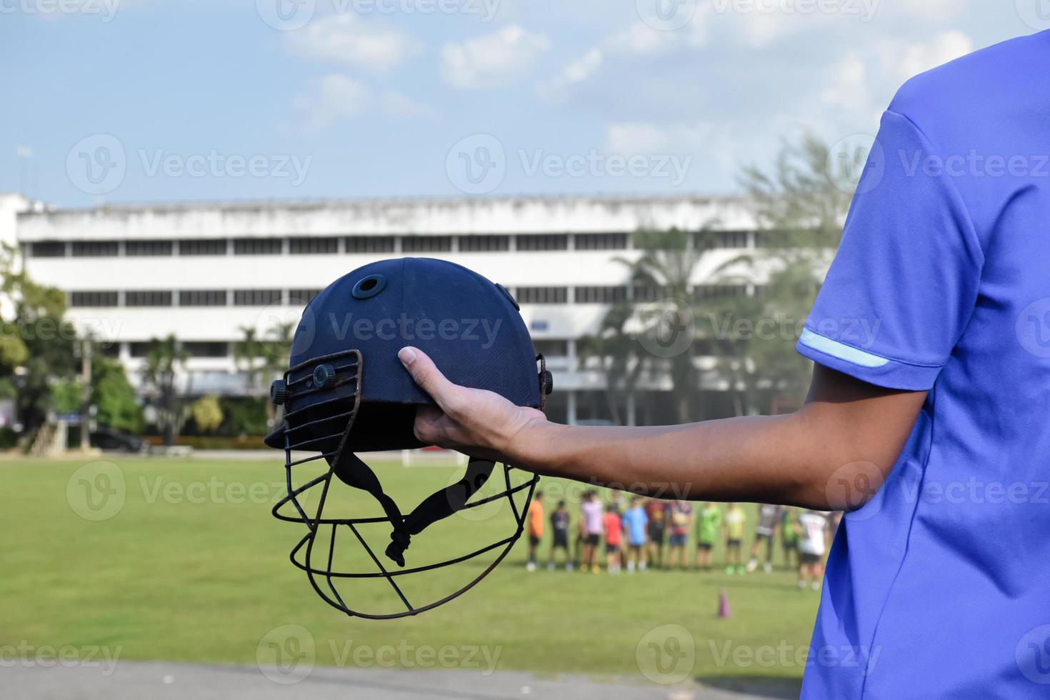 Cricket helmet holding in hand of cricketer, blurred green grass cricket field, concept for using cricket sport equipment in training. photo
