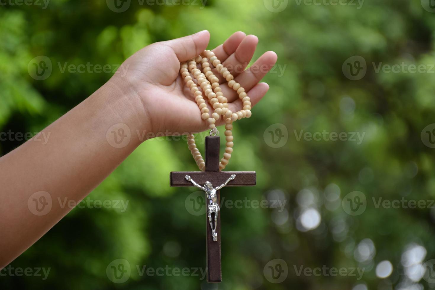 Wooden cross bead necklace holding in hands, natural blurr bokeh background, soft and selective focus. photo