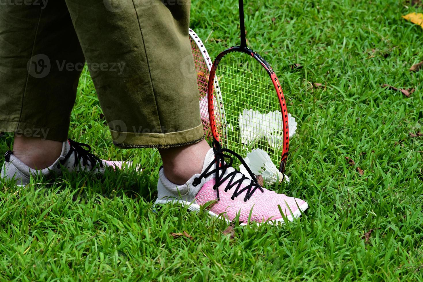 Closeup view of asian female sport shoes, badminton rackets and shuttlecocks on green grass lawn, outdoor badminton playing in freetimes and afterwork with other people concept. photo