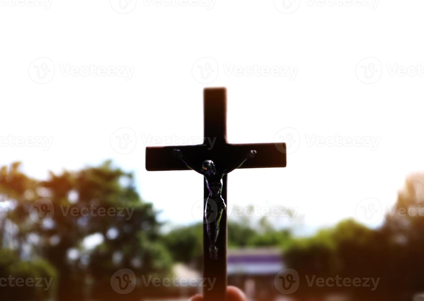A black wooden cross with a statue of Jesus crucified by his arm. Behind it is the school building of a school in an Asian country, soft and selective focus. photo