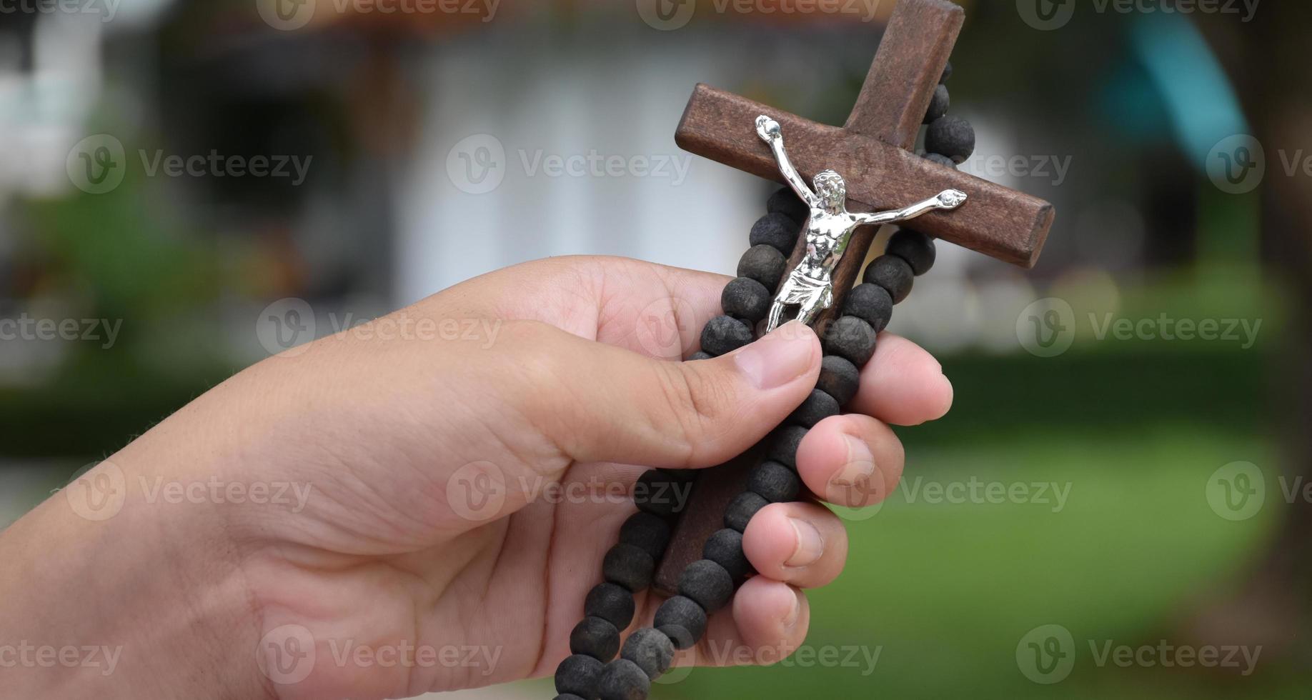 Wooden cross and wooden rosary are held in hands of young asian Catholic prayer while praying in the temple park area. photo