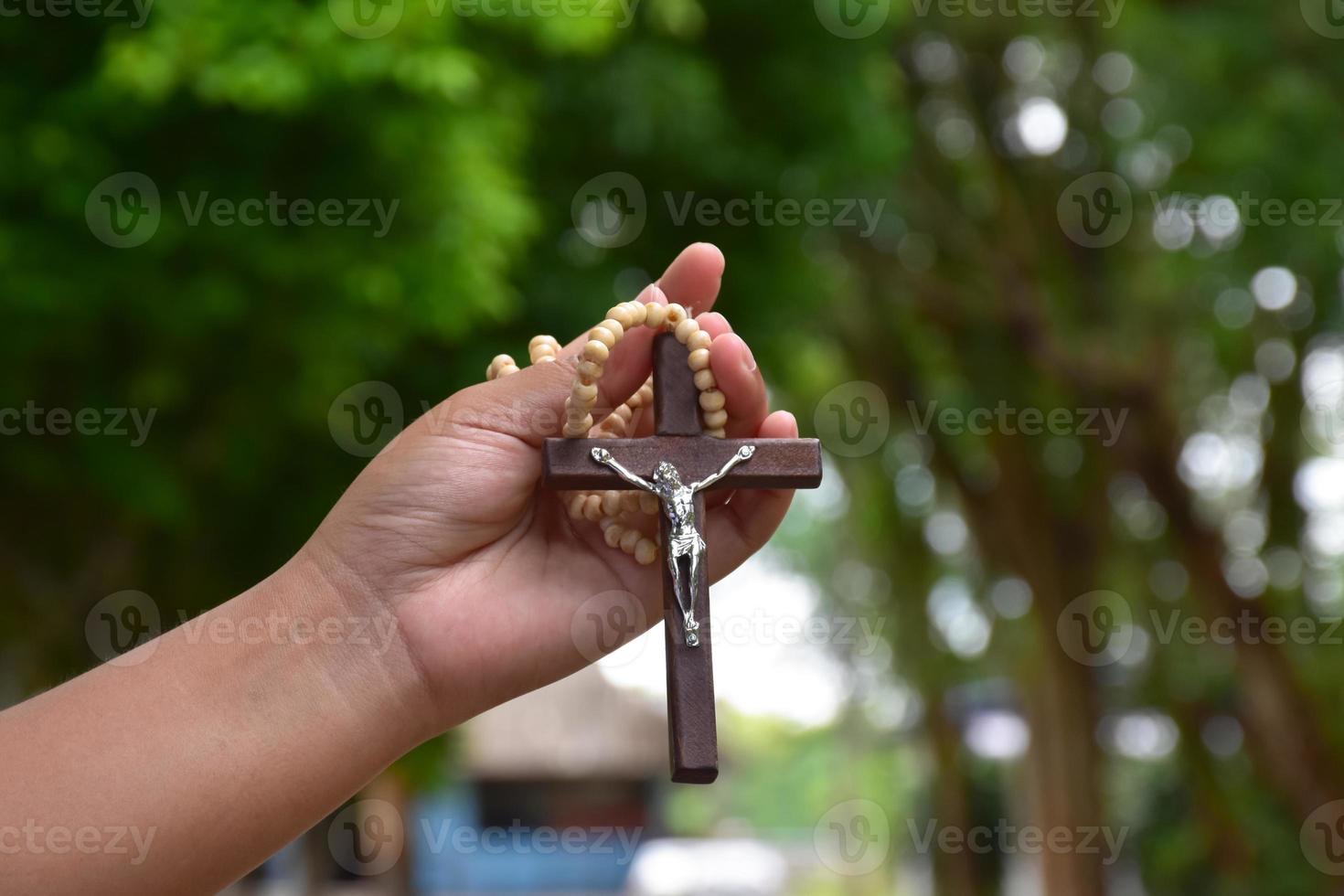 Wooden cross bead necklace holding in hands, natural blurr bokeh background, soft and selective focus. photo