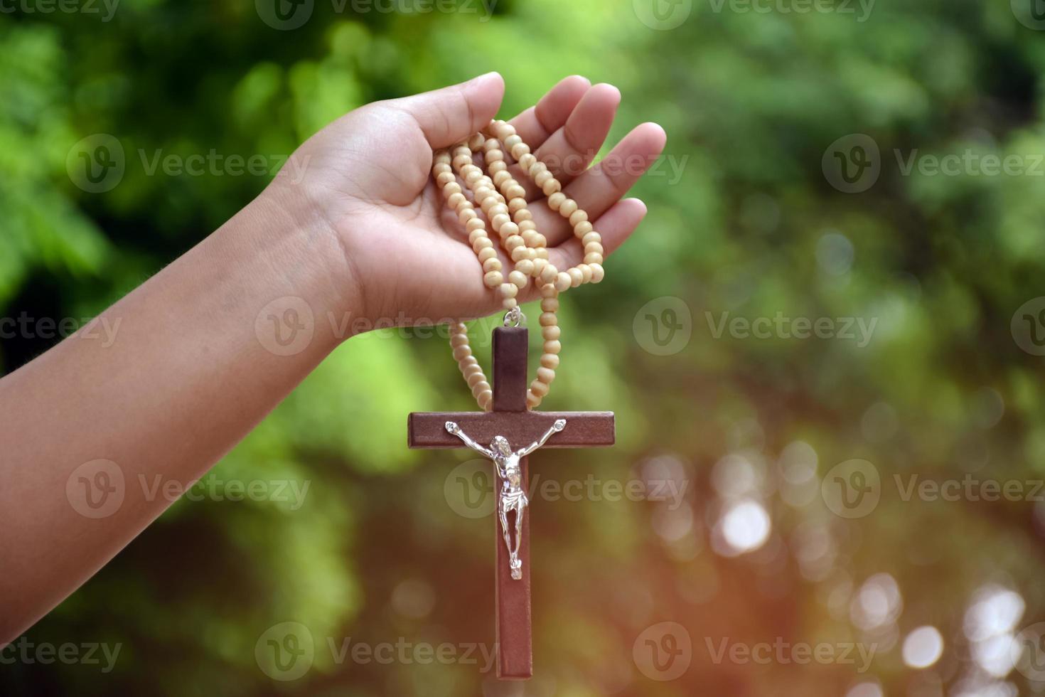 Wooden cross bead necklace holding in hands, natural blurr bokeh background, soft and selective focus. photo