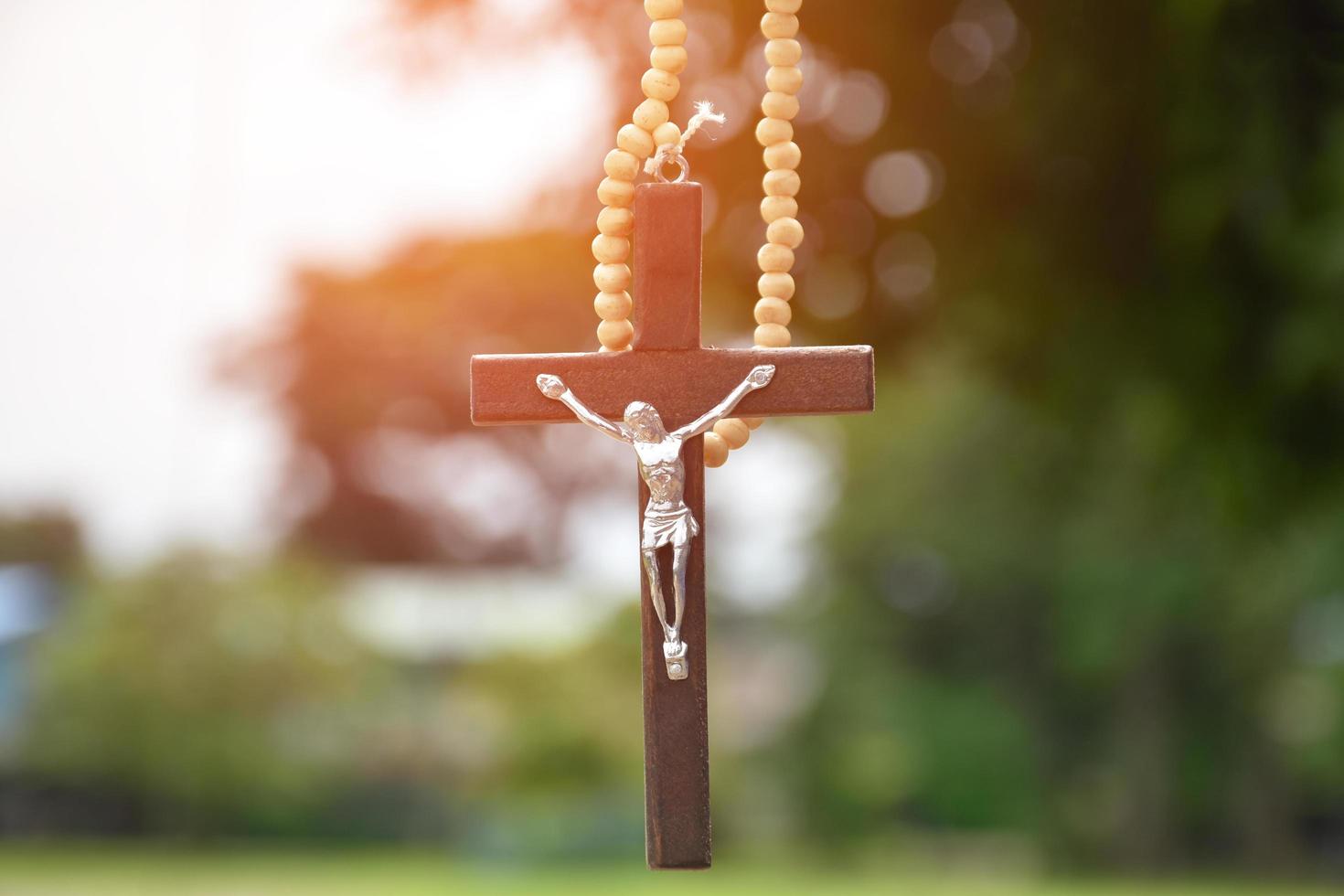 Wooden cross bead necklace hanging, natural blurr bokeh trees background, soft and selective focus. photo