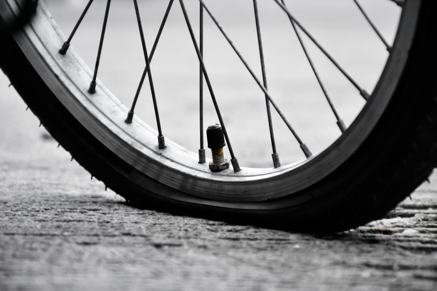 Rear wheel of bike which is flat and parked on the pavement beside the road. photo