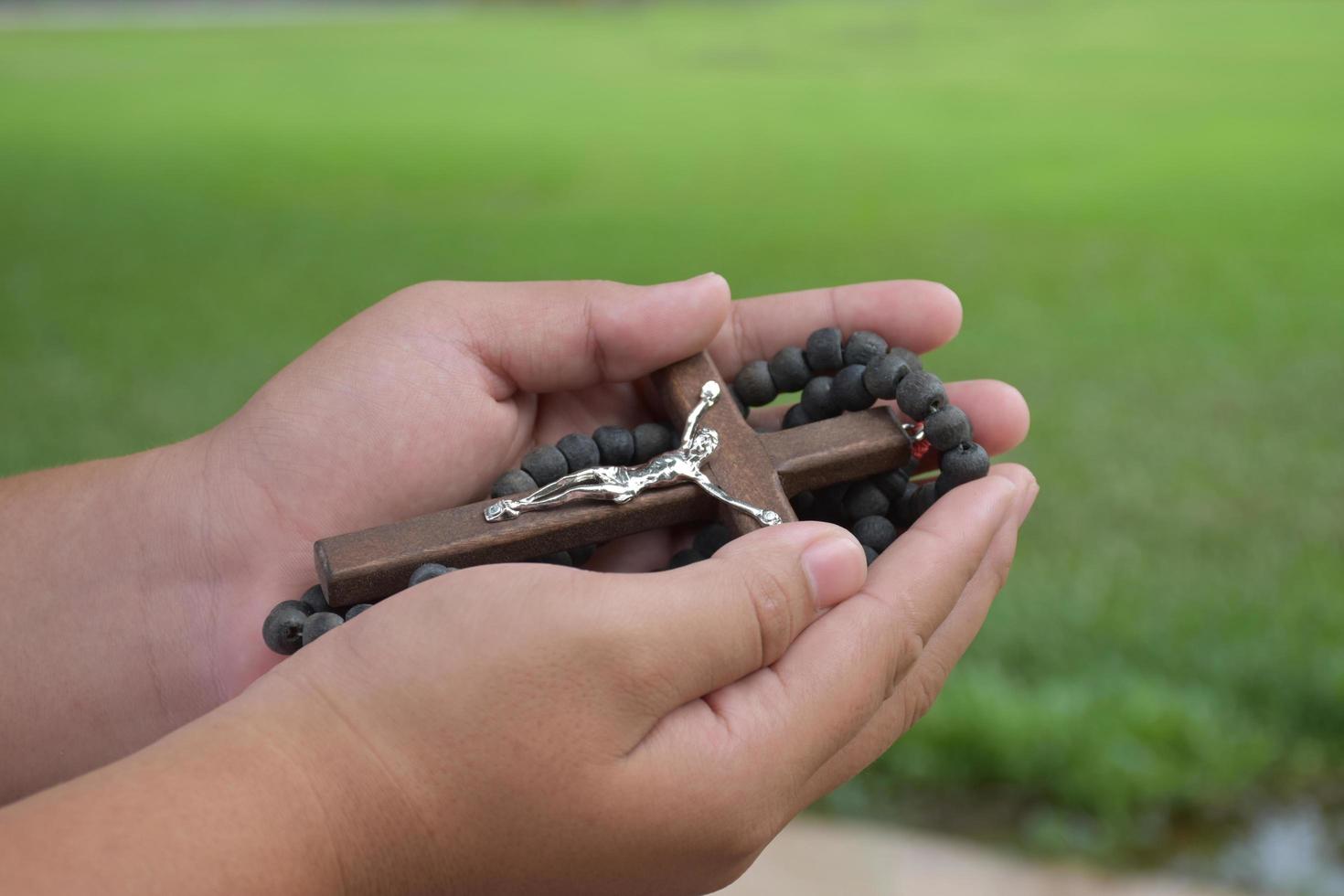 Wooden cross and wooden rosary are held in hands of young asian Catholic prayer while praying in the temple park area. photo