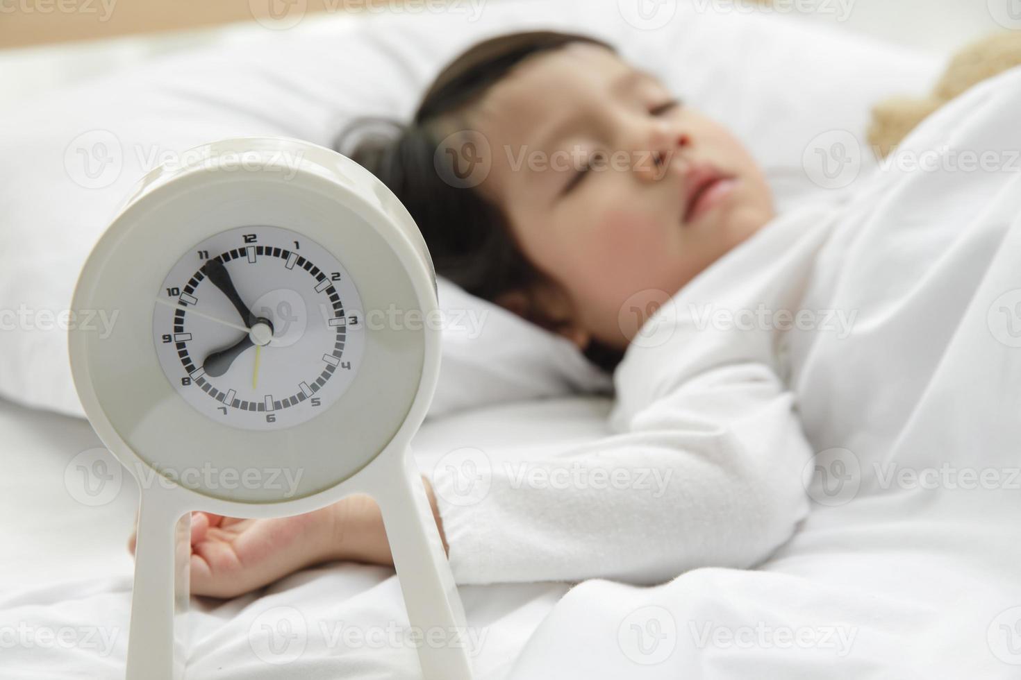 Child girl sleeping with alarm clock on the wooden bed in her bedroom, Happy asian child little girl and alarm clock wake up in the morning photo