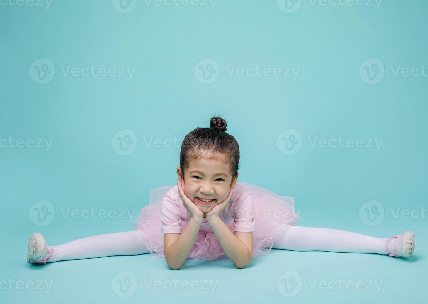 Beautiful smiling Asian little girl in a pink suit is dancing a ballet at school, empty space in studio shot isolated on colorful blue background photo