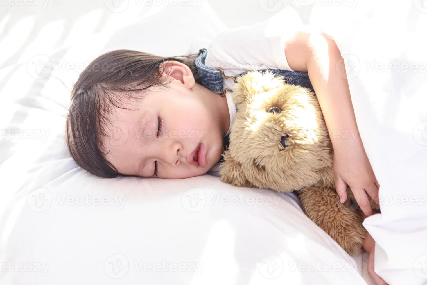 Little asian girl sleeping with her toy teddy bear photo