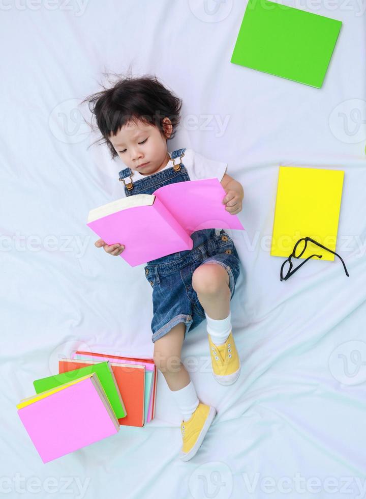 niña pequeña asiática o una linda niña asiática leyendo un libro en la cama foto