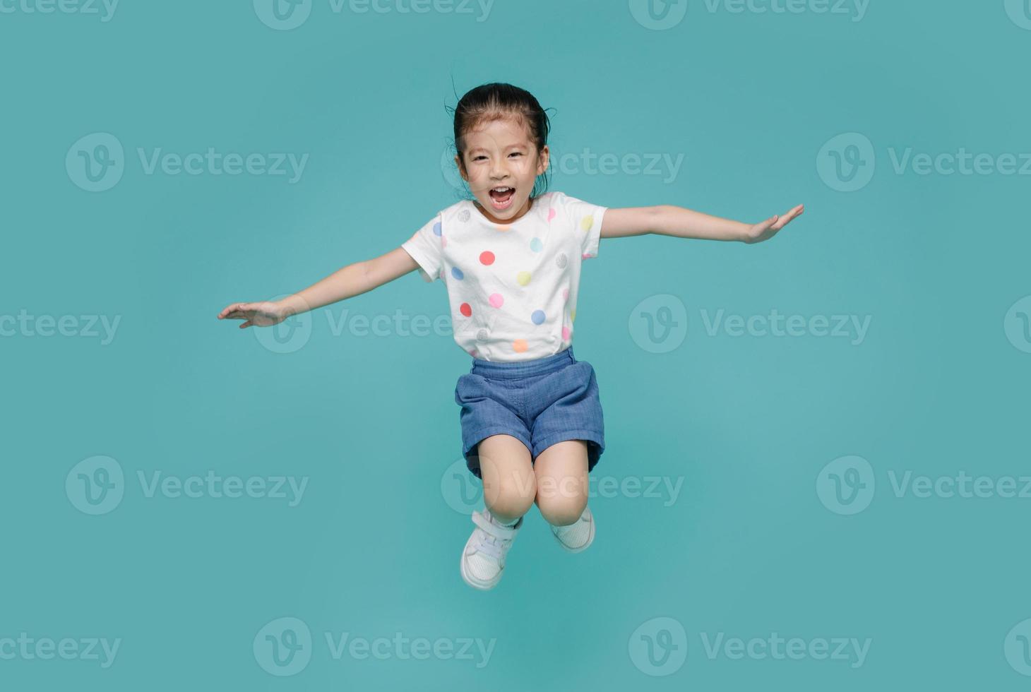 Excited Asian little girl jumping in mid-air, empty space in studio shot isolated on colorful blue background photo