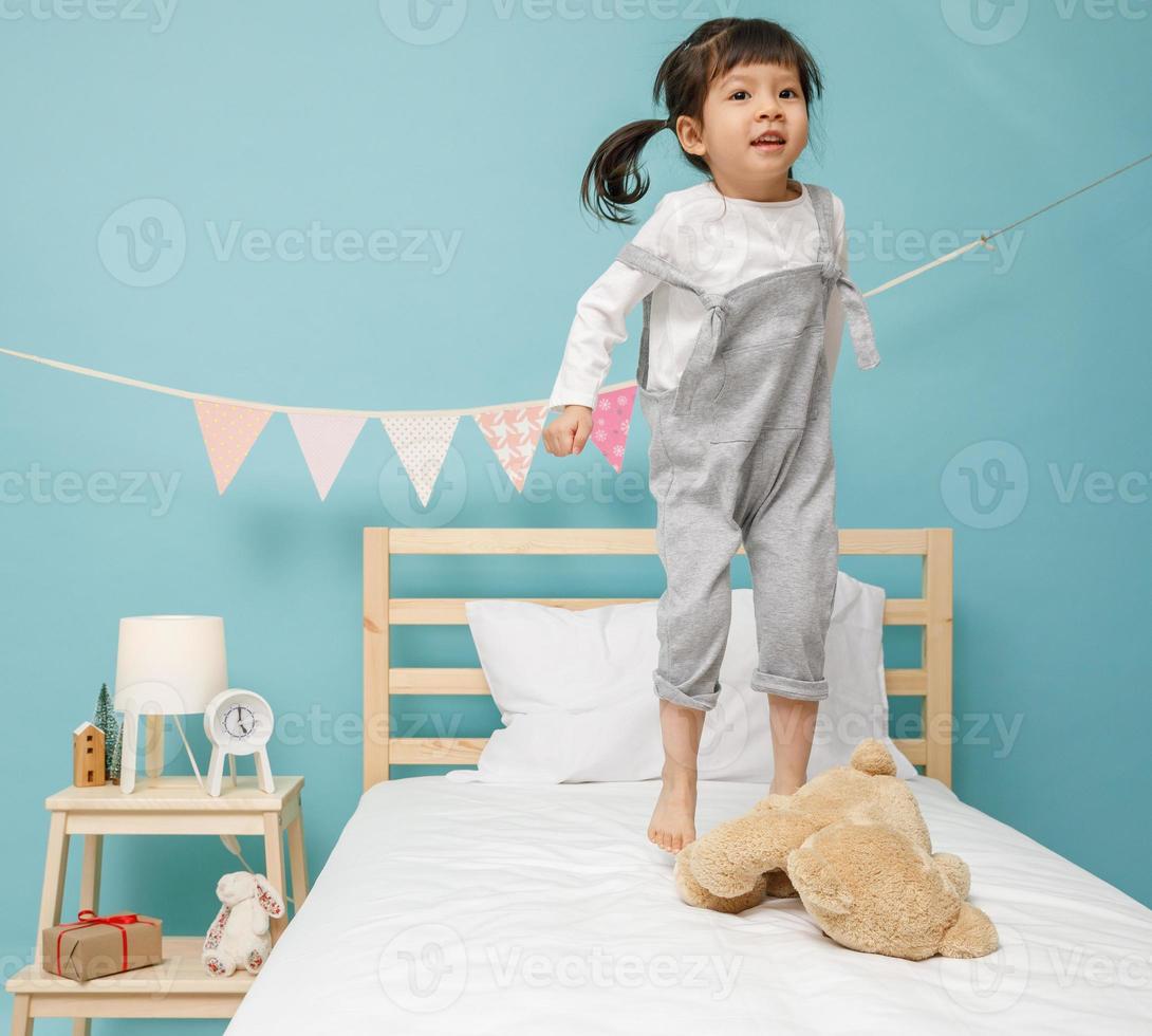 Child girl playing on the wooden bed in her bedroom, Happy asian child little girl jumping on the bed, happy family concept photo