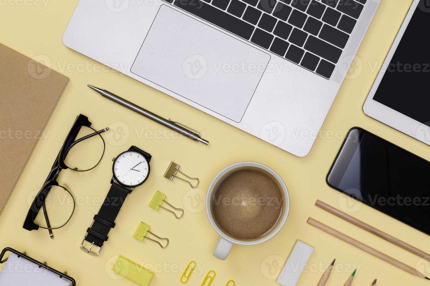 diseño plano creativo de maqueta de suministros de oficina con cuaderno, taza de café caliente, tableta, teléfono inteligente, anteojos, libros y accesorios aislados en fondo amarillo, espacio de trabajo para el concepto de autónomo foto